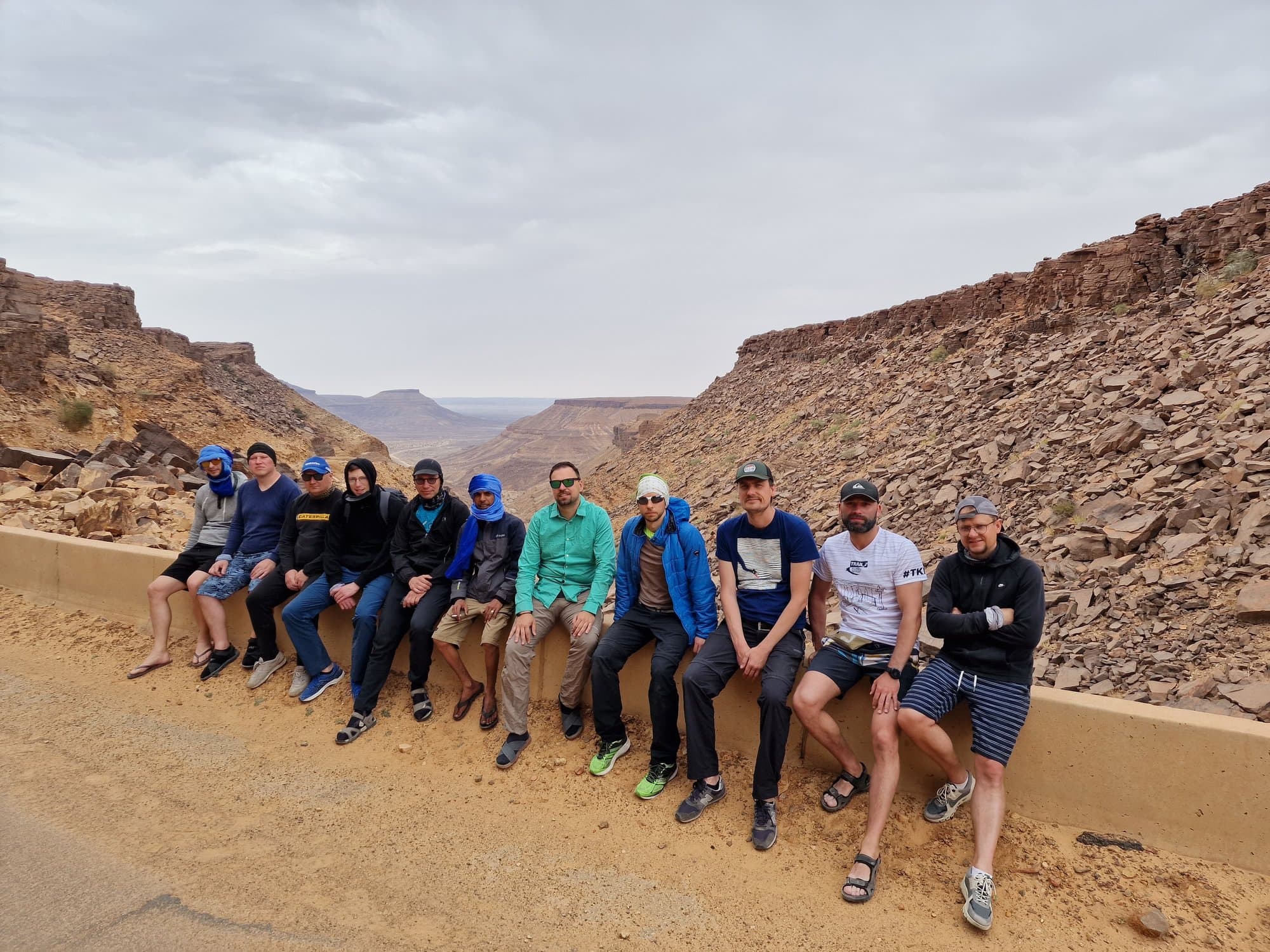 The group resting on a canyon pass road wall in the Adrar