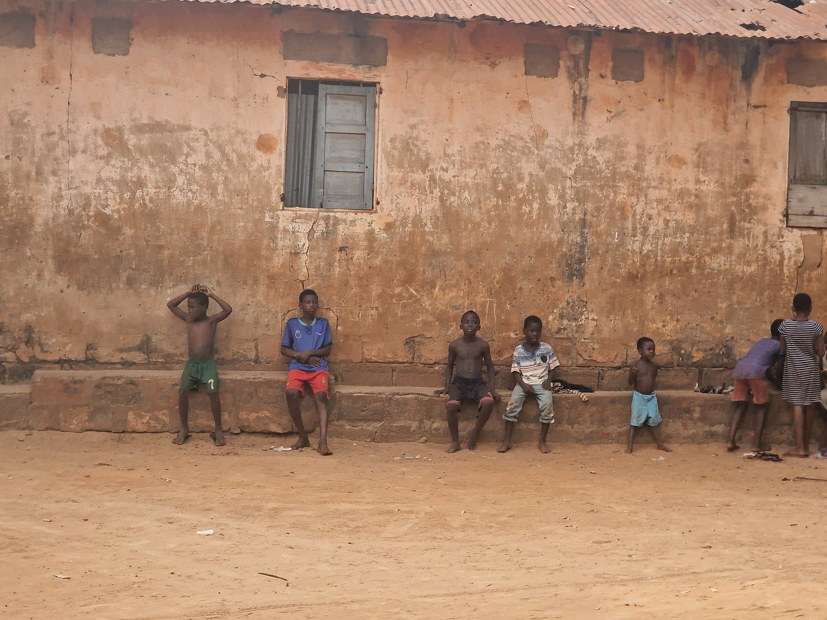 Children sitting along the base of an ochre wall in Togoville, Togo