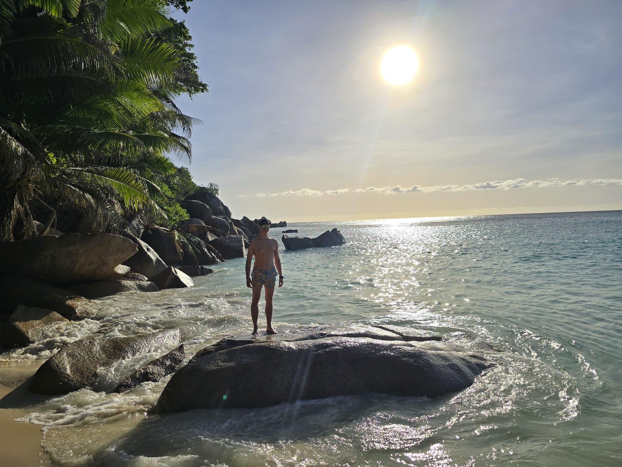 Standing on a rock in the shallows under a high sun at Anse Georgette, Praslin, Seychelles