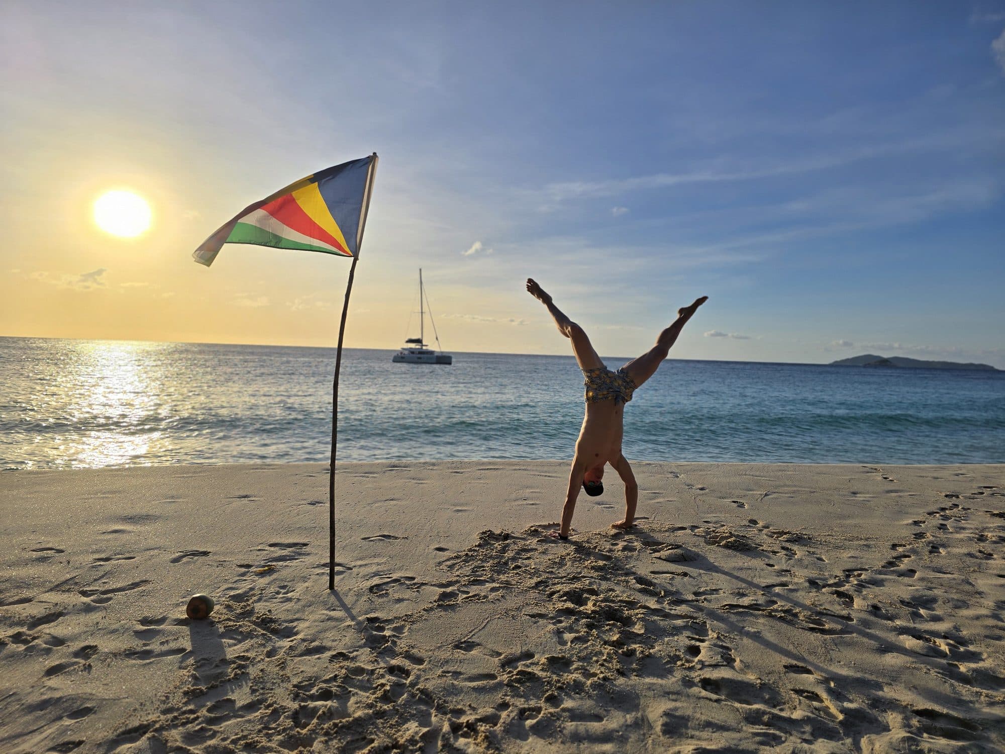 A handstand on the sand at sunset beside a Seychelles flag, Anse Georgette, Praslin