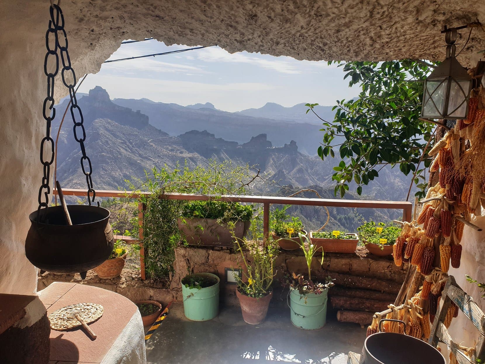 A cave-house balcony at Artenara with plants, corn and a kettle over the mountain view, Gran Canaria
