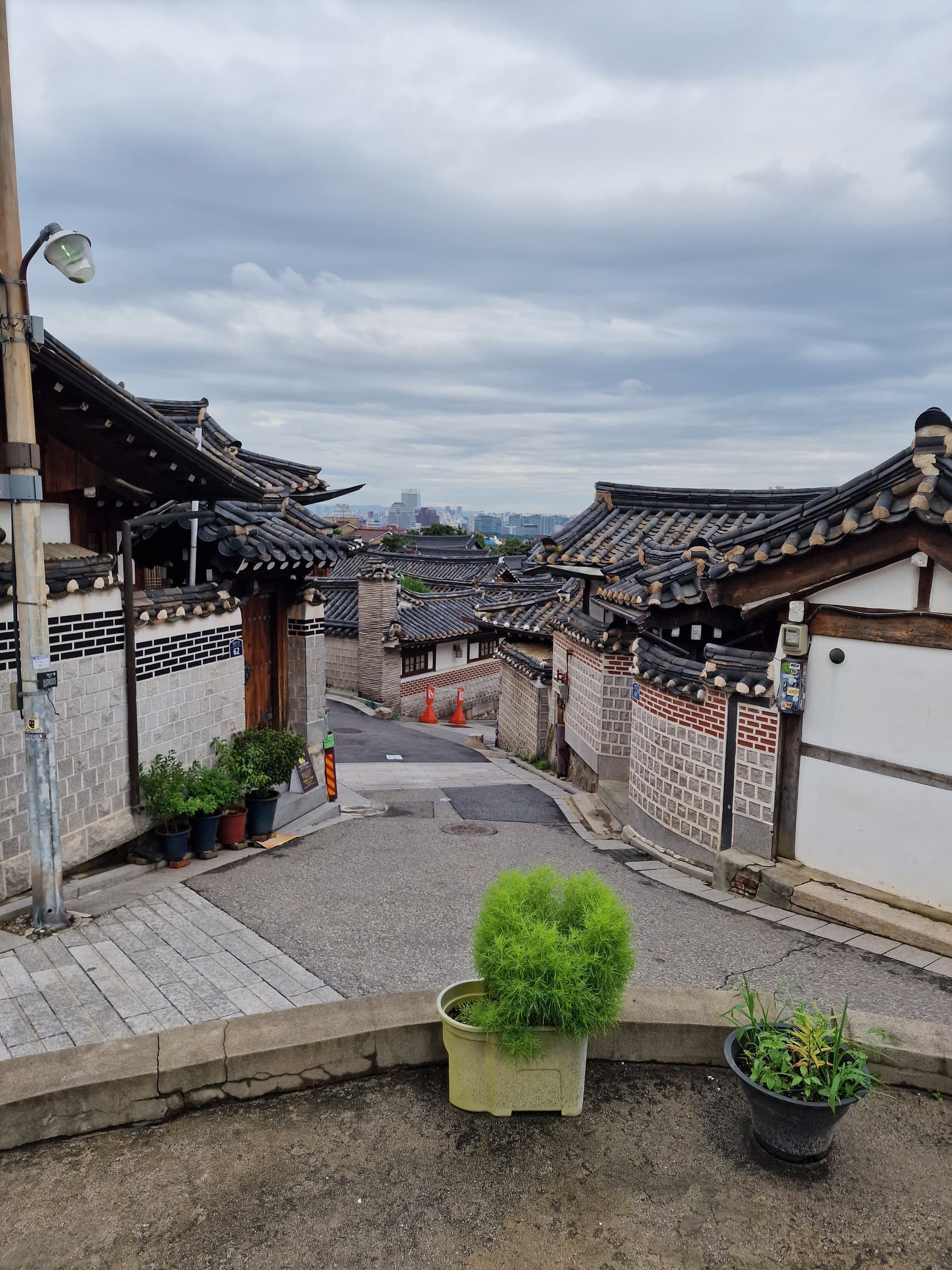 A lane of hanok houses in Bukchon with tiled roofs and the modern skyline beyond, Seoul