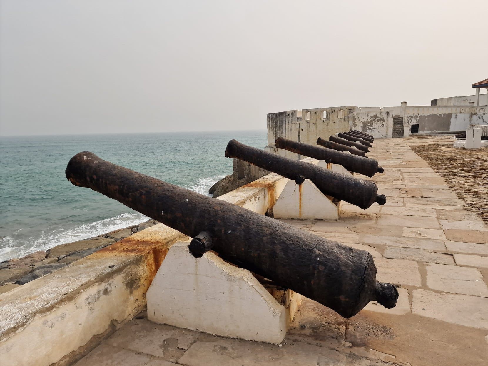 An iron cannon on the whitewashed rampart of Cape Coast Castle pointing out to sea, Ghana