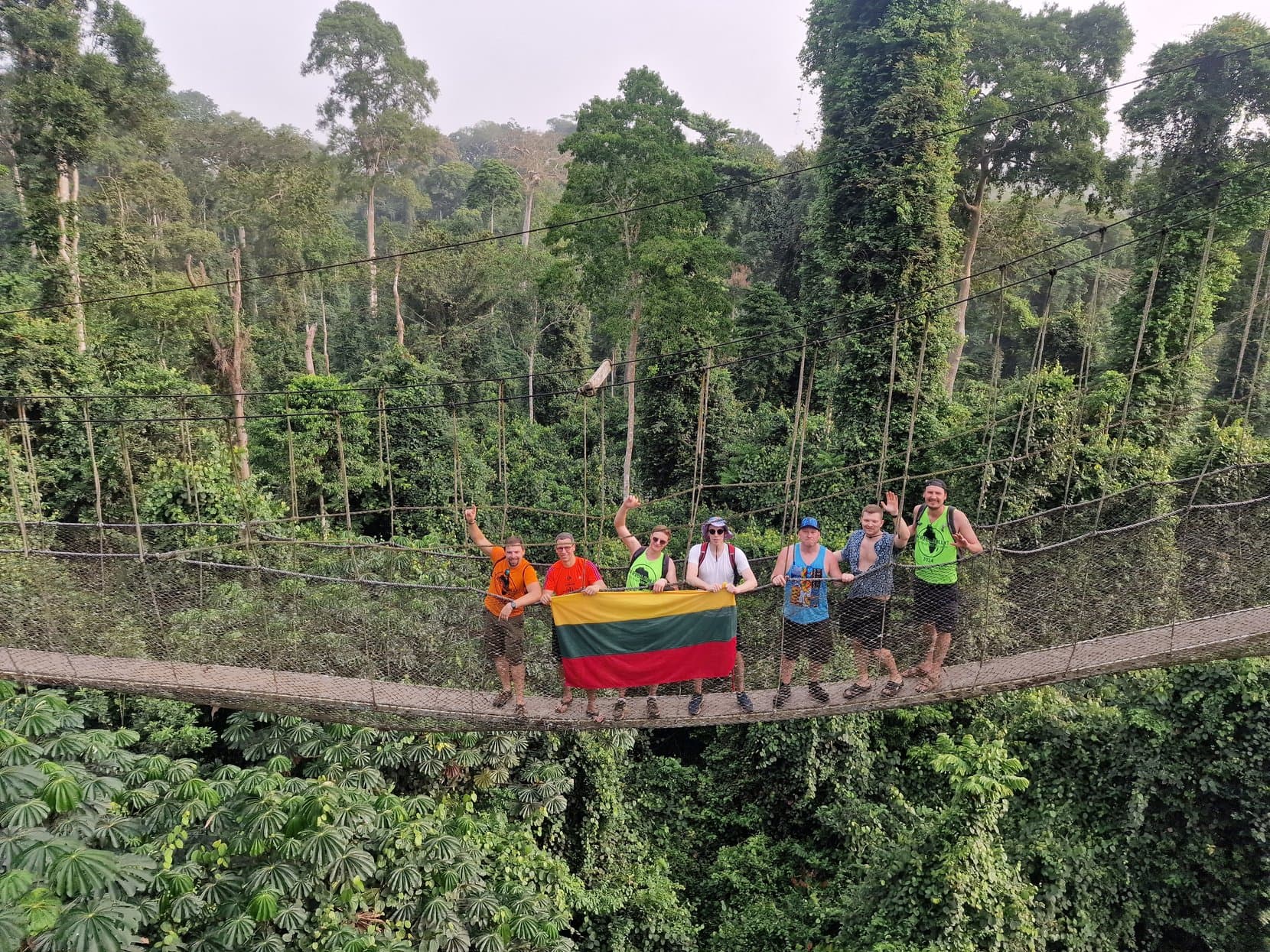 The rally crew holding a Lithuanian flag on a rope bridge above the rainforest canopy at Kakum, Ghana