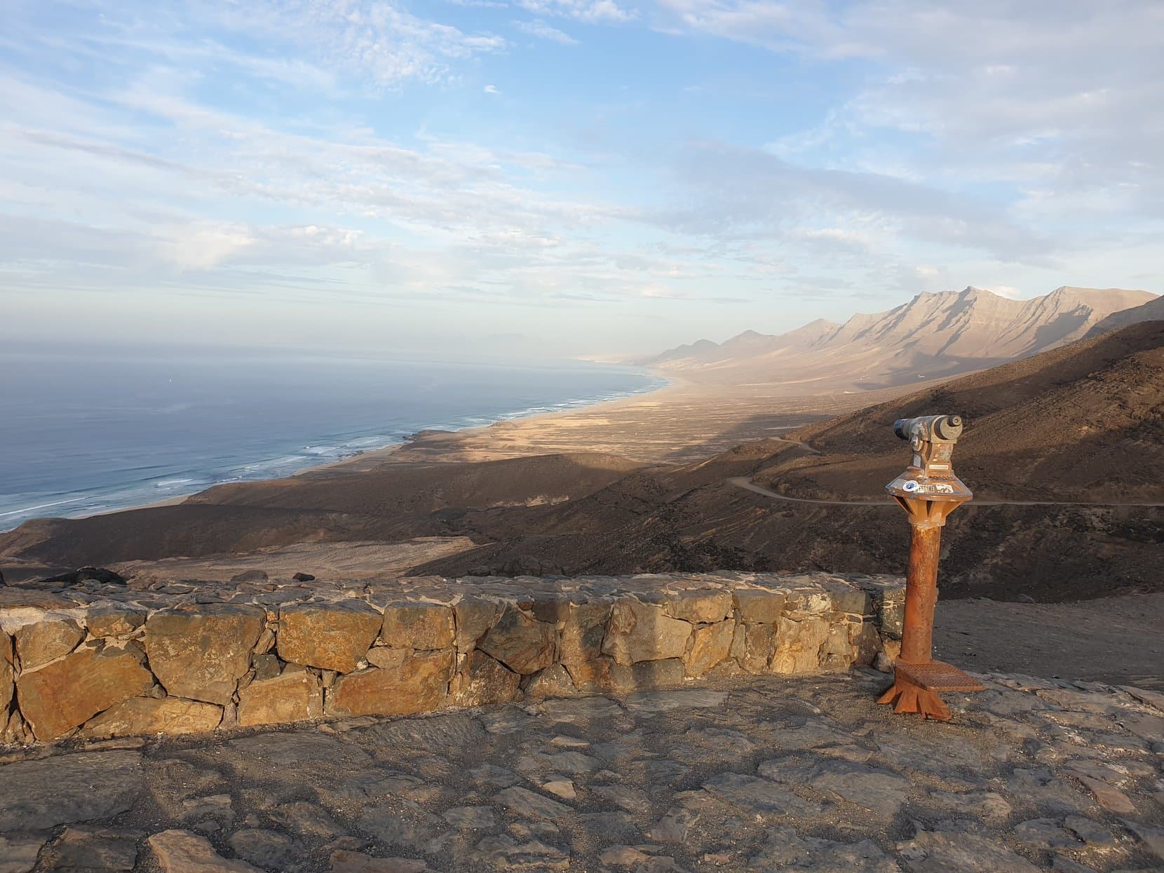 Cofete beach and the Jandía mountain wall at golden hour, from the mirador's stone wall with its old telescope, Fuerteventura