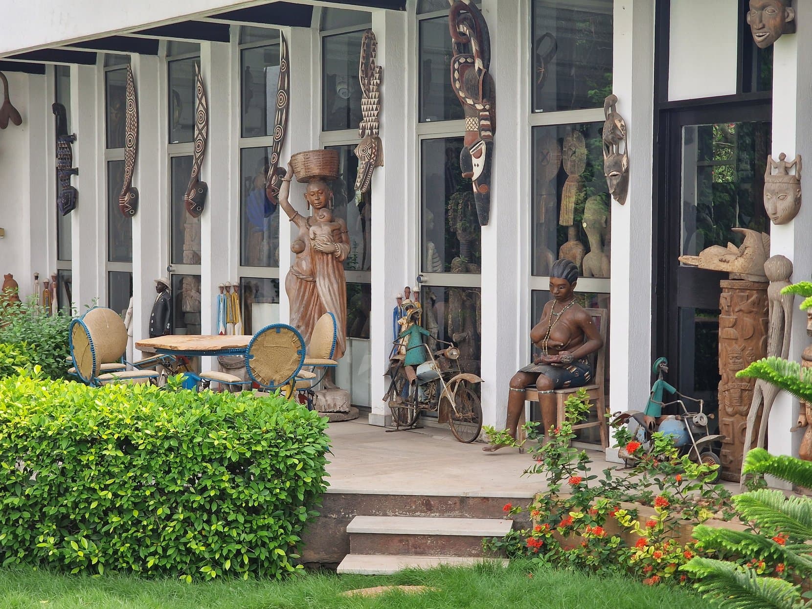 Tall carved wooden figures along the colonnade of a museum with people sitting beneath them, Lomé, Togo
