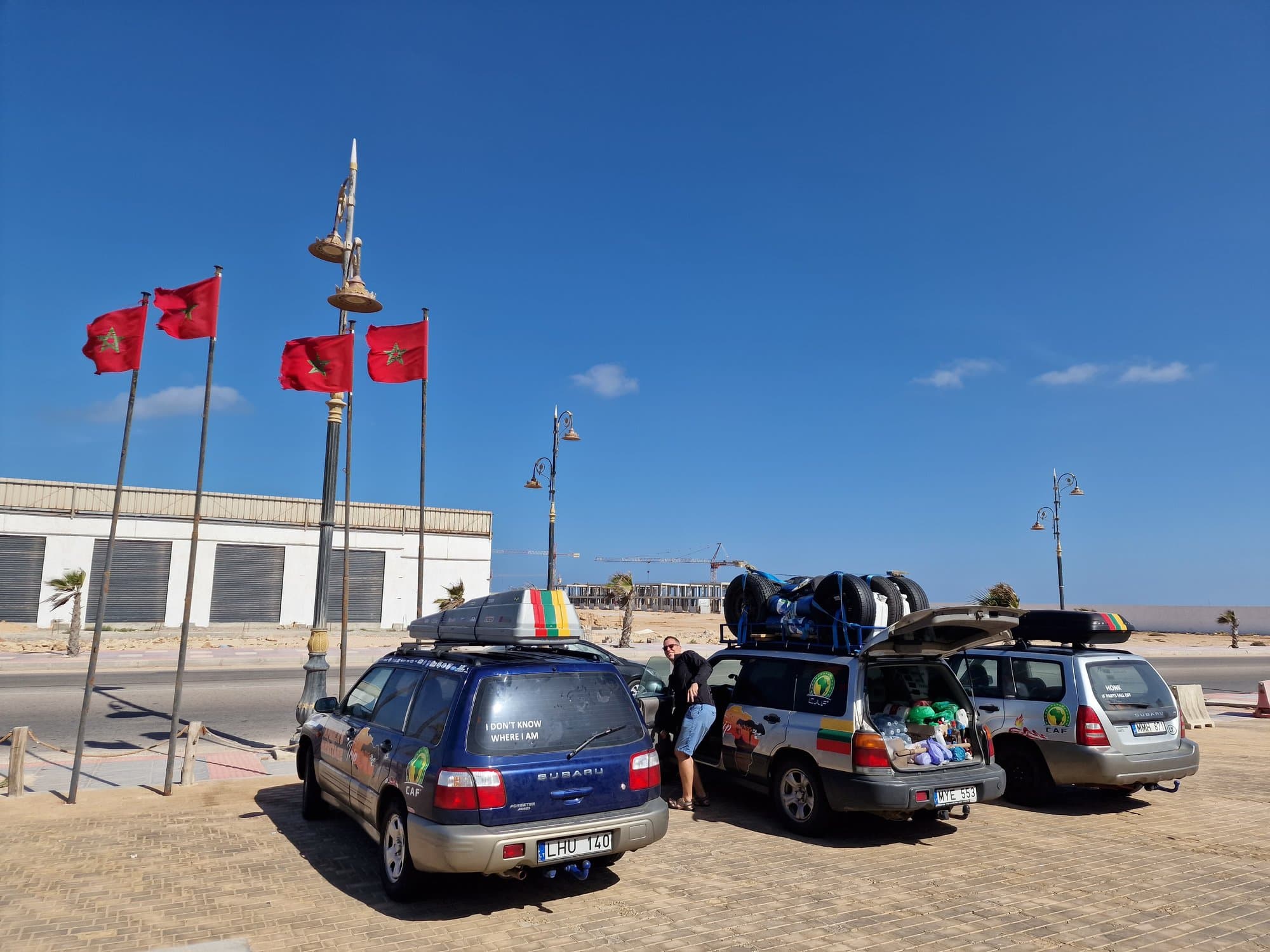 Rally cars parked beneath a row of Moroccan flags on Dakhla's seafront