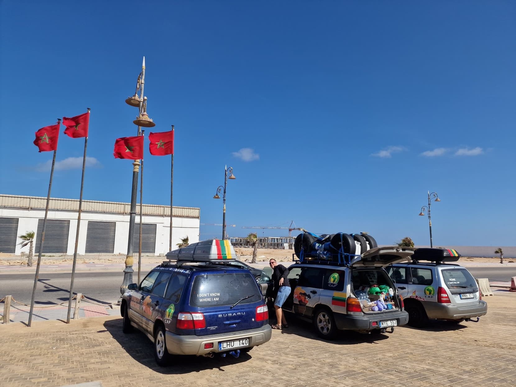 Rally cars parked beneath a row of Moroccan flags on Dakhla's seafront