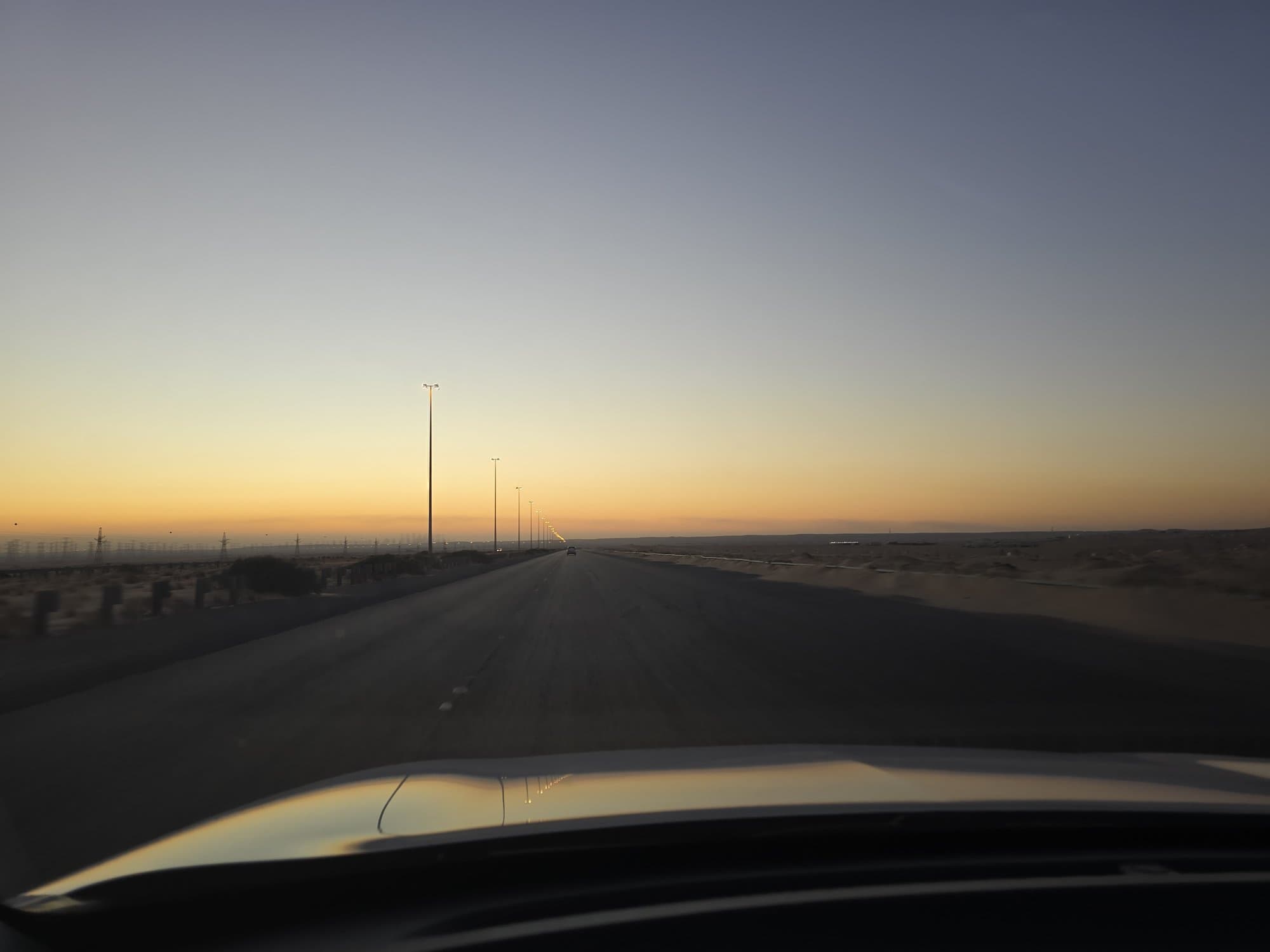 The desert highway at dusk from the car, power lines running to the horizon