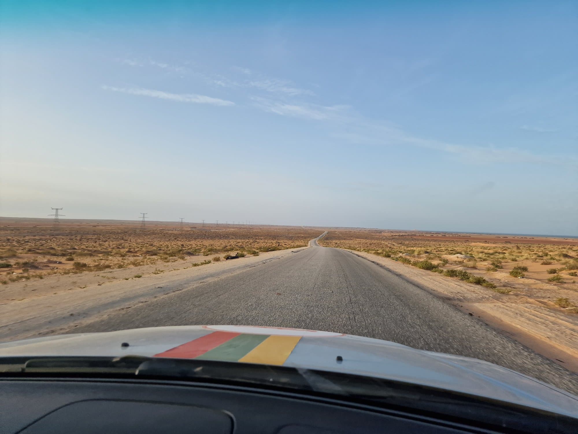 A straight desert highway at dawn seen over the car bonnet
