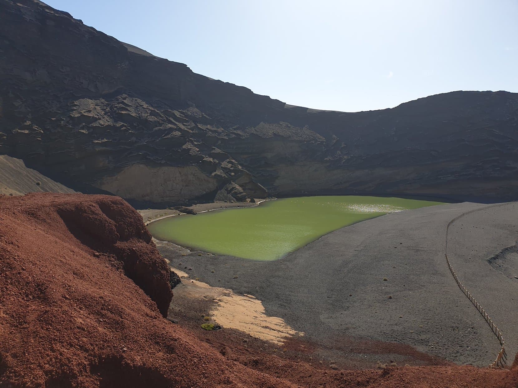 The green lagoon of El Golfo behind its black beach, under a red volcanic crater wall, Lanzarote