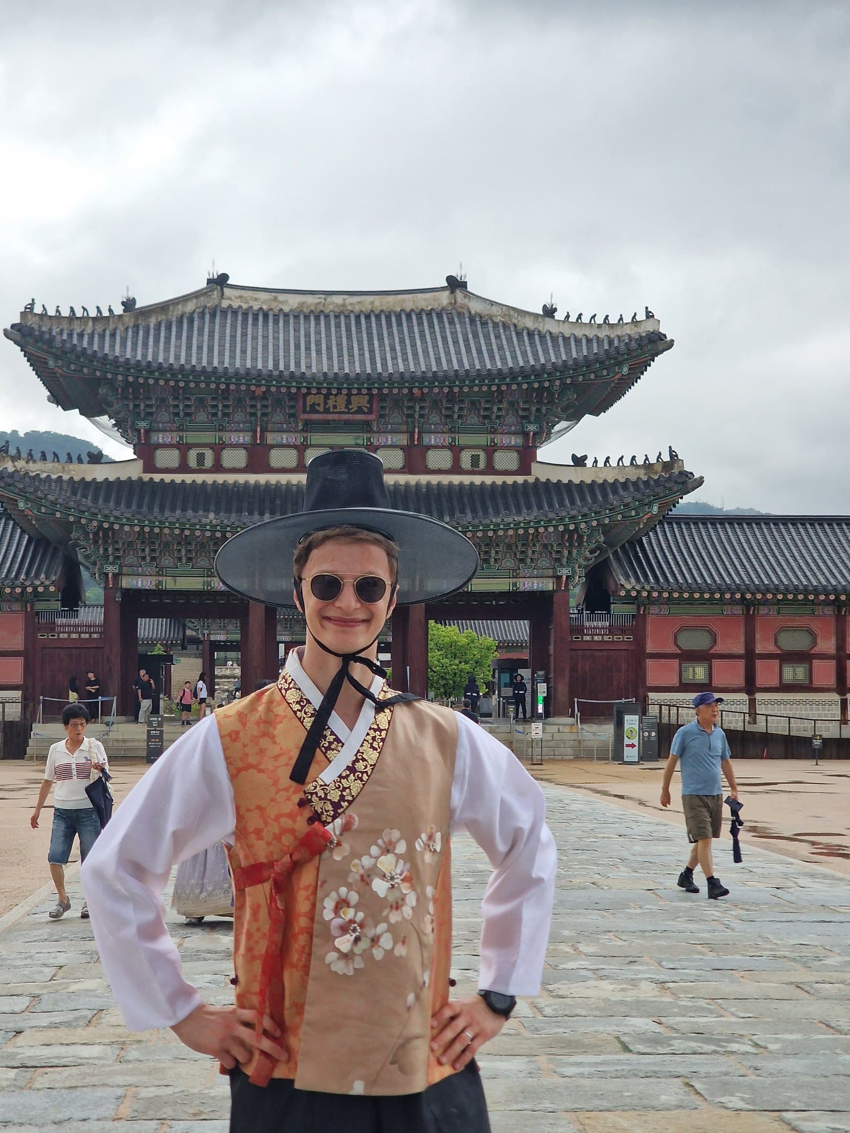 A man in a peach hanbok and wide black gat hat in front of Heungnyemun gate at Gyeongbokgung, Seoul