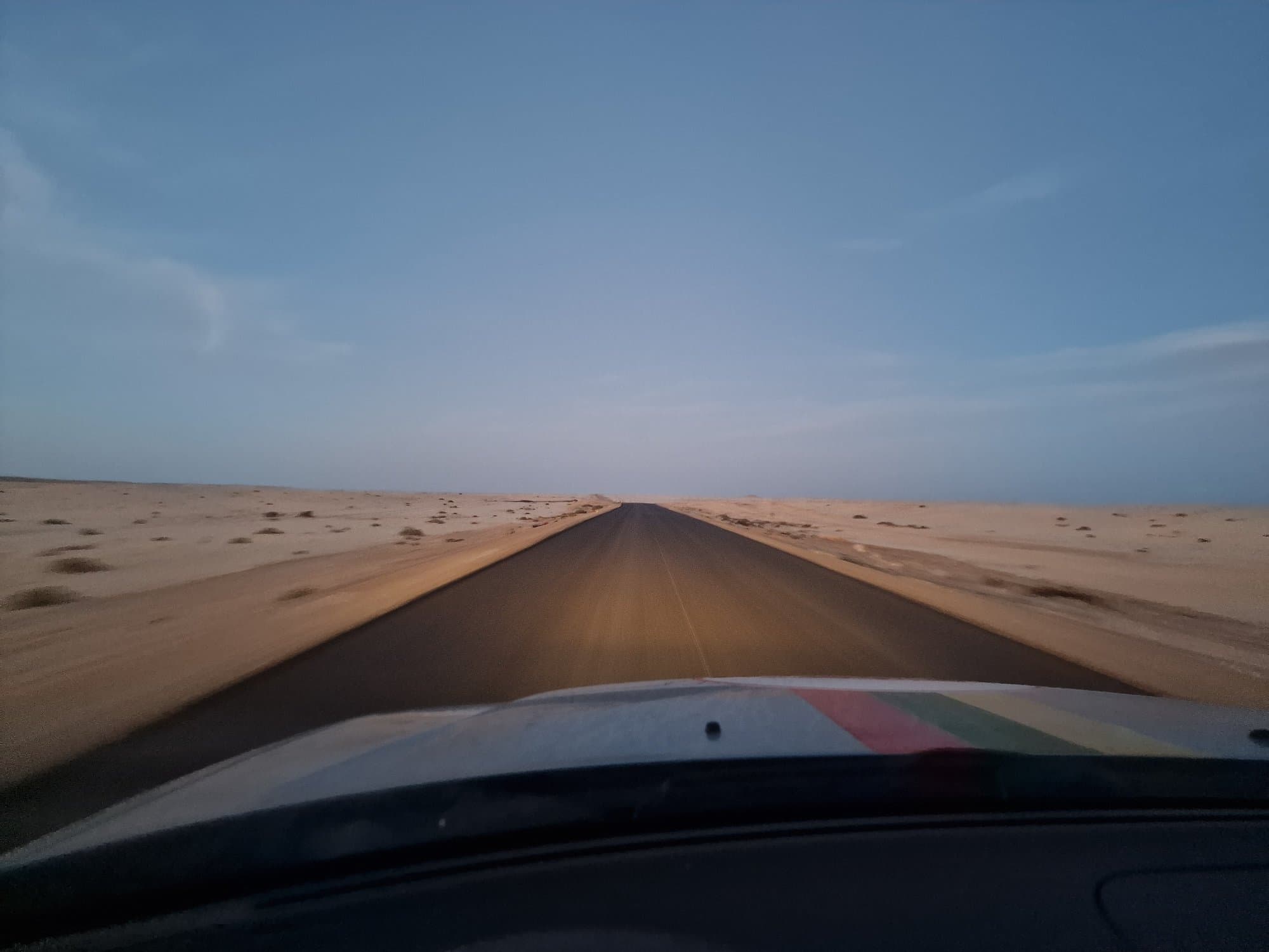 The empty desert highway seen over the car bonnet, a dune encroaching from the left