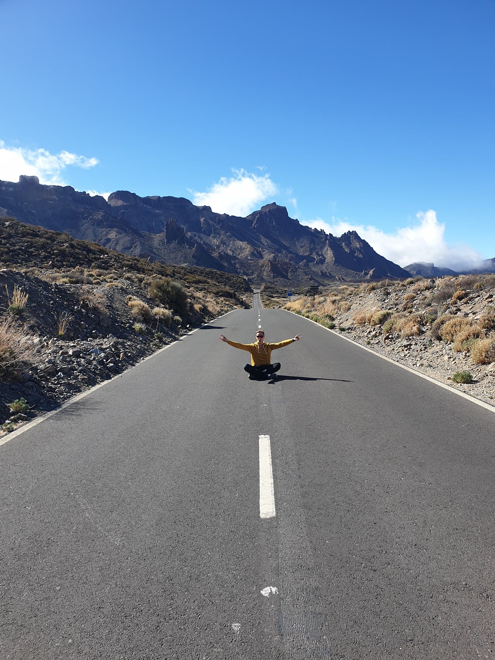 The founder sitting in the middle of an empty mountain road below dark crags, Tenerife