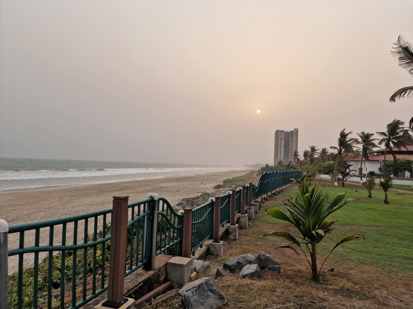 A railing above the beach at dusk with a tower block beyond, Accra, Ghana