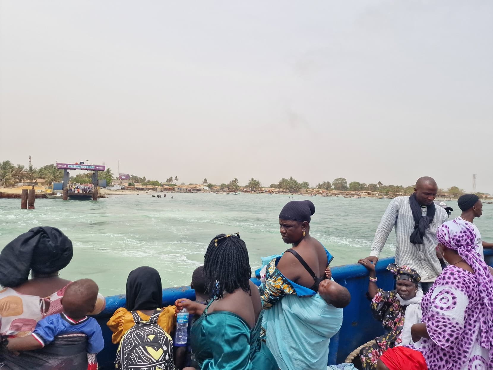 Passengers at the ferry rail crossing the Gambia River mouth toward Banjul