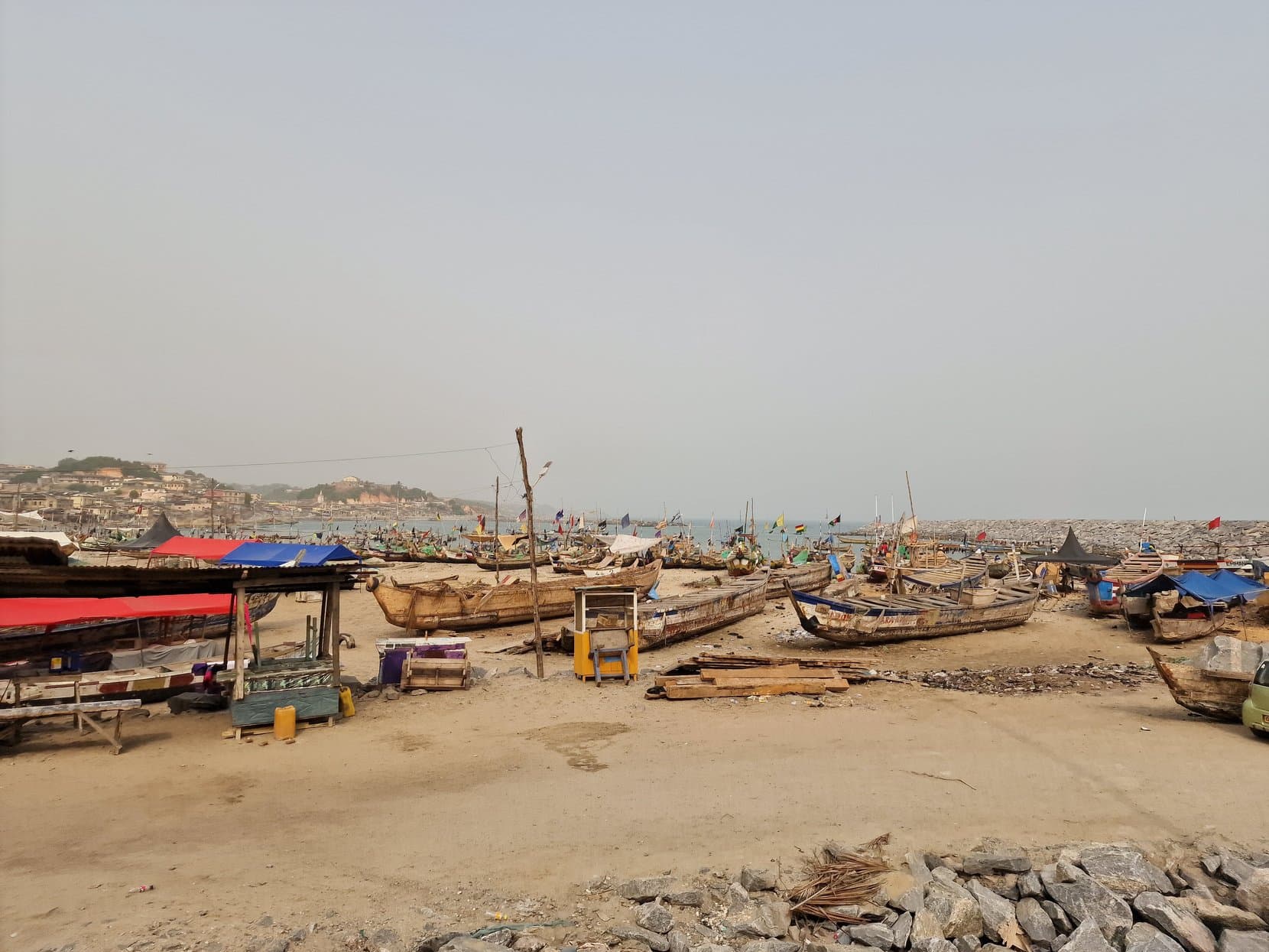 Wooden fishing boats and stalls on the beach directly below the castle walls, Cape Coast, Ghana