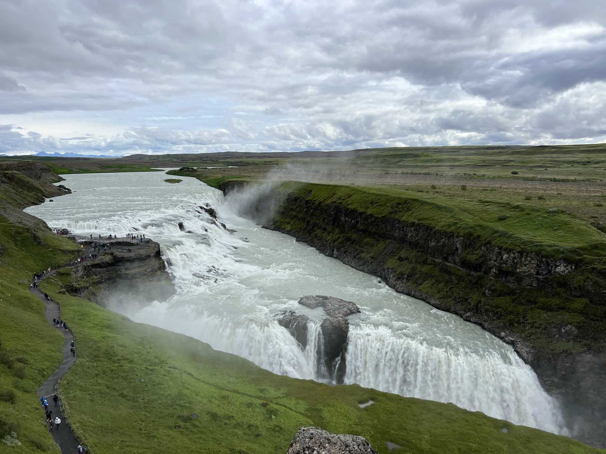 Gullfoss dropping into its canyon with spray rising over green fields