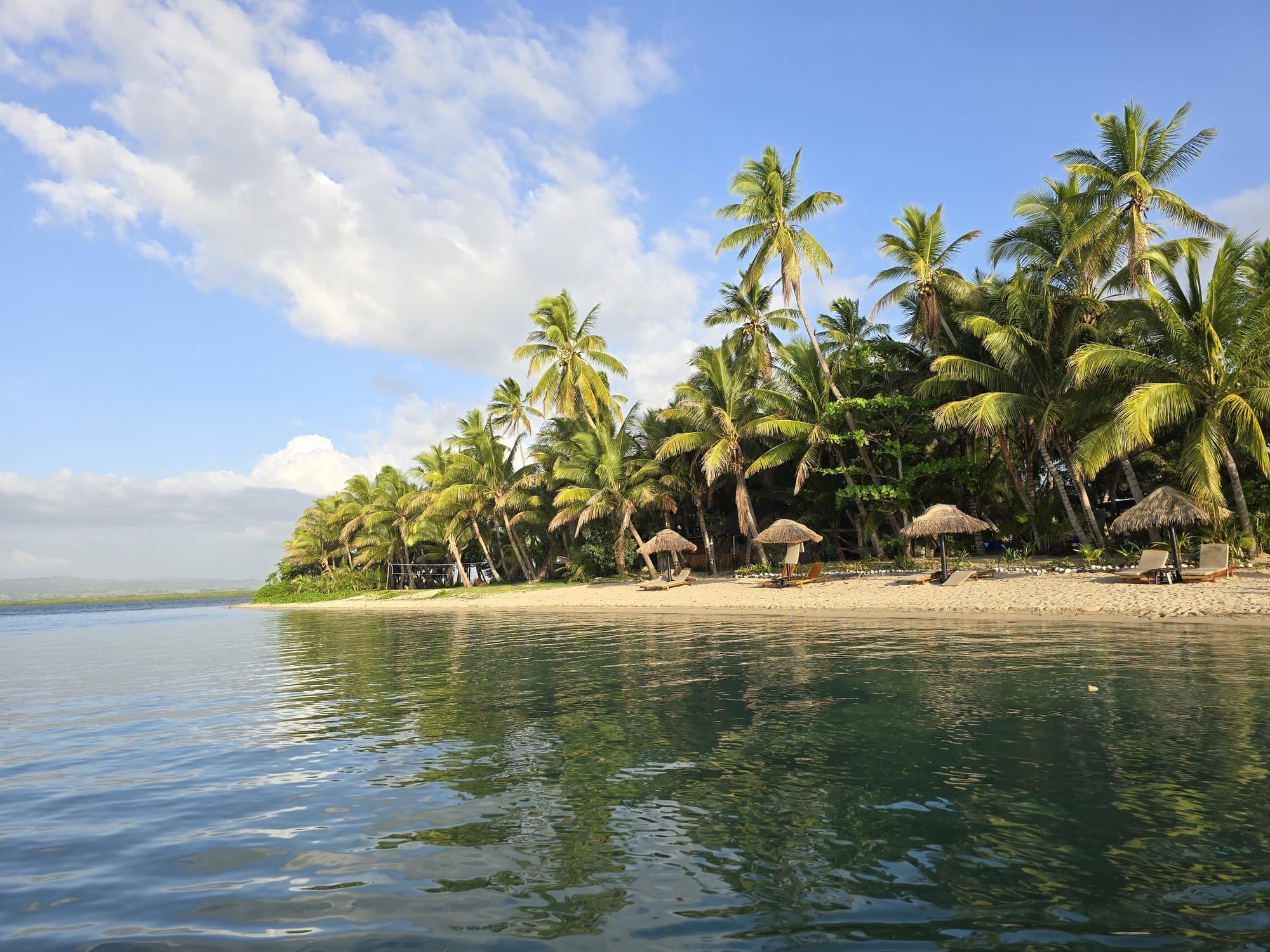 An island resort beach with thatched umbrellas and calm green-blue water
