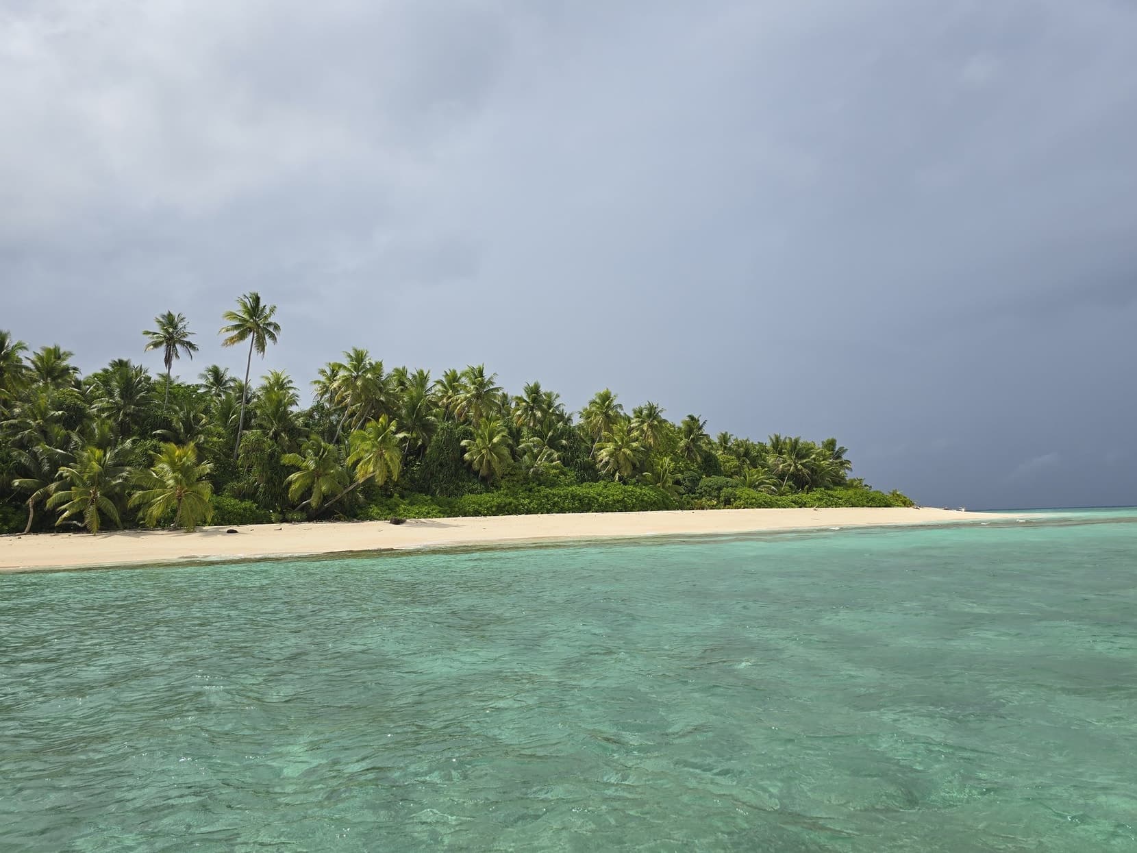 A lagoon islet's white beach and palms seen from the water, nobody on it