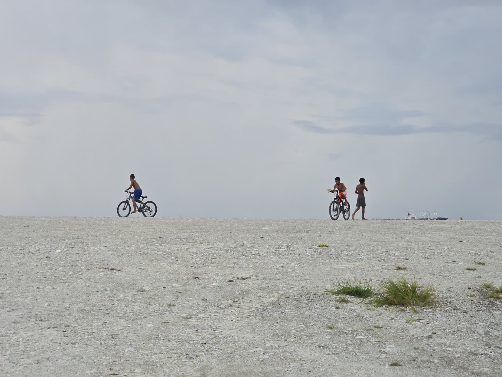 Two kids cycling across the bare coral flat under a huge sky