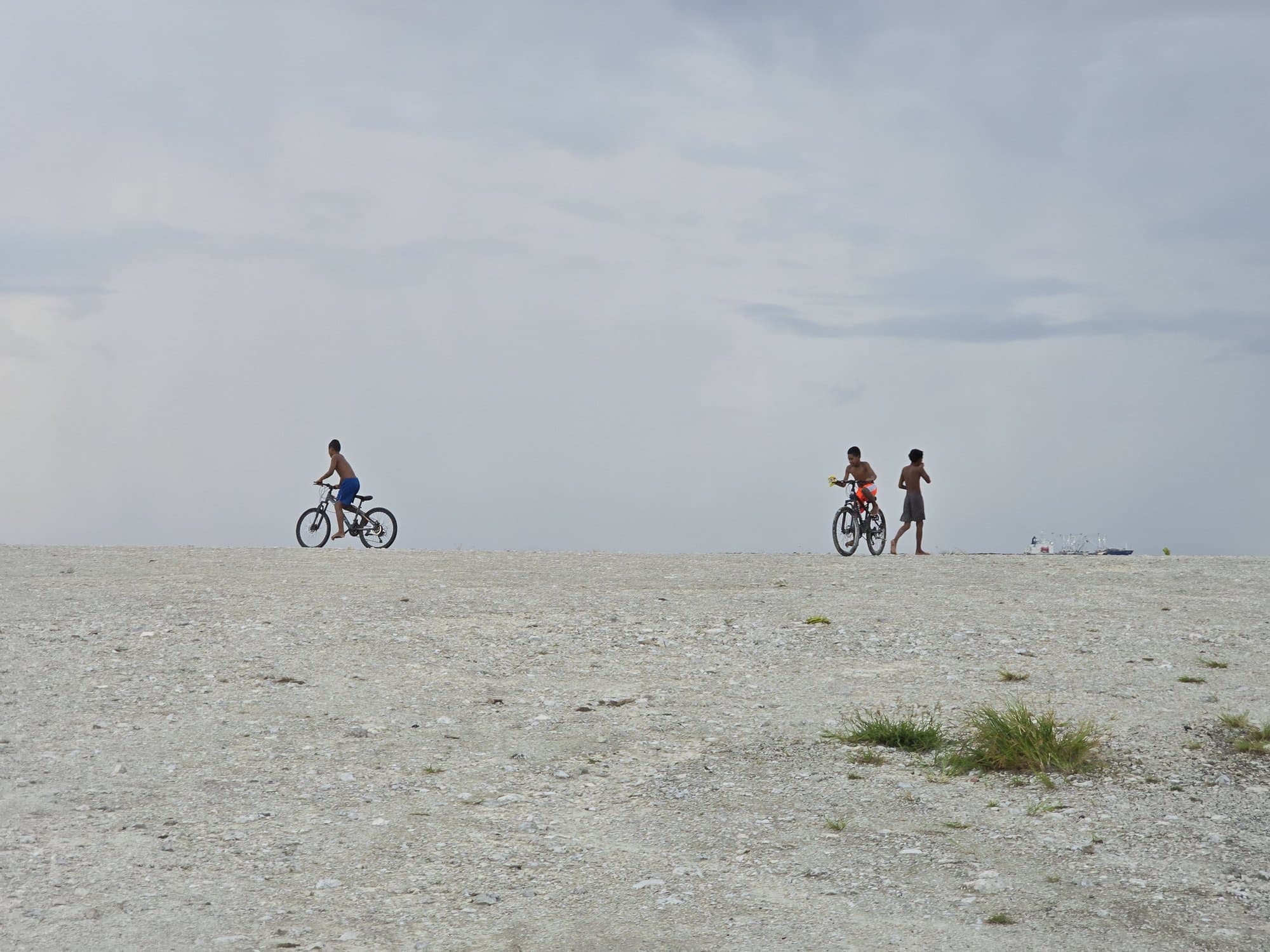 Two kids cycling across the bare coral flat under a huge sky