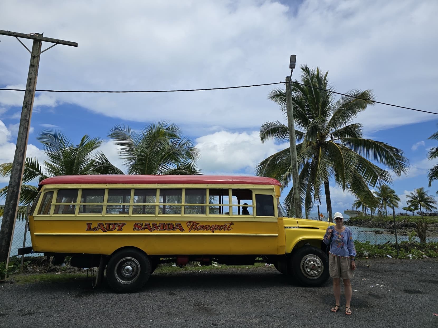 A yellow Lady Samoa wooden island bus parked under palms