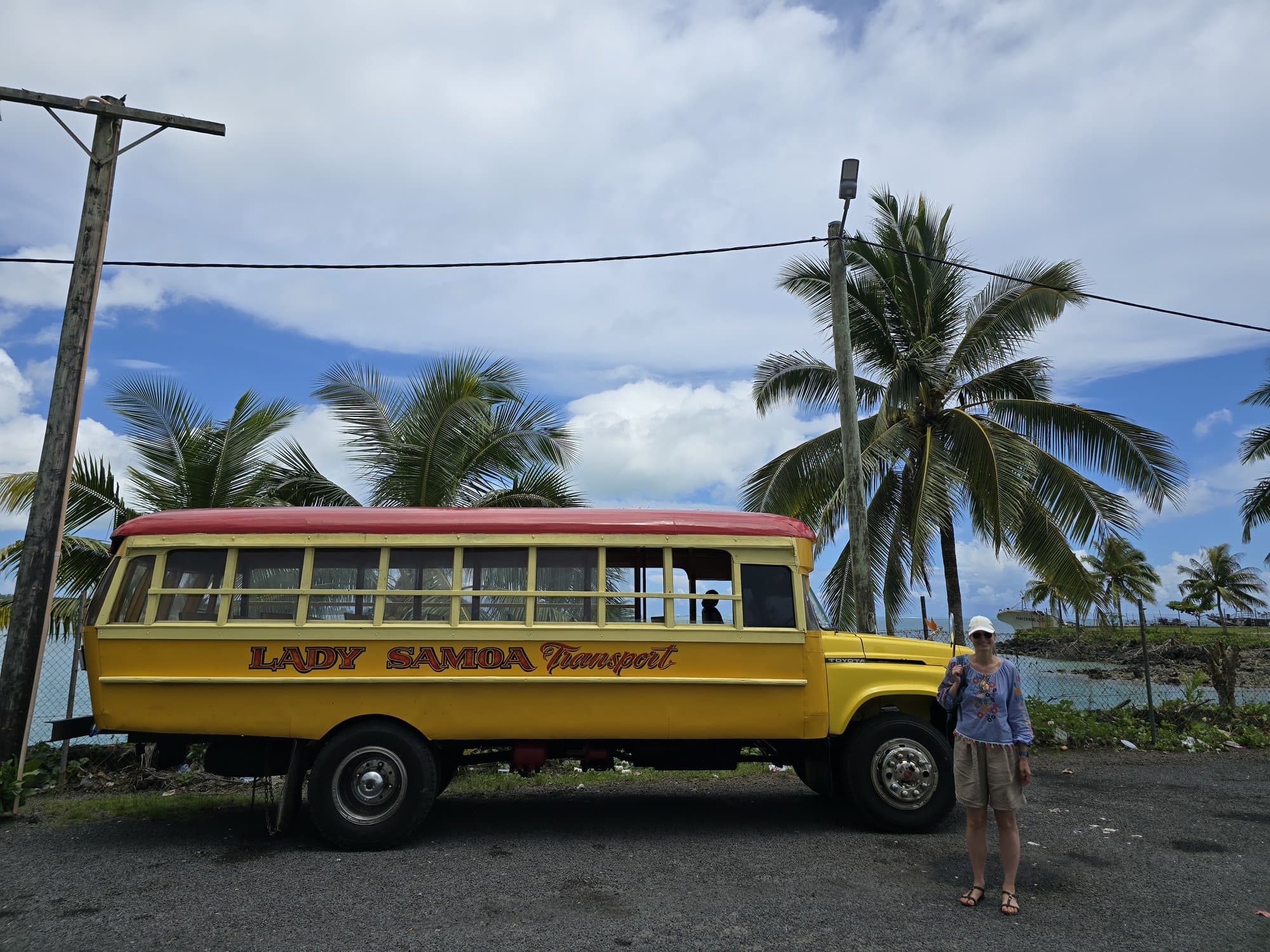 A yellow Lady Samoa wooden island bus parked under palms