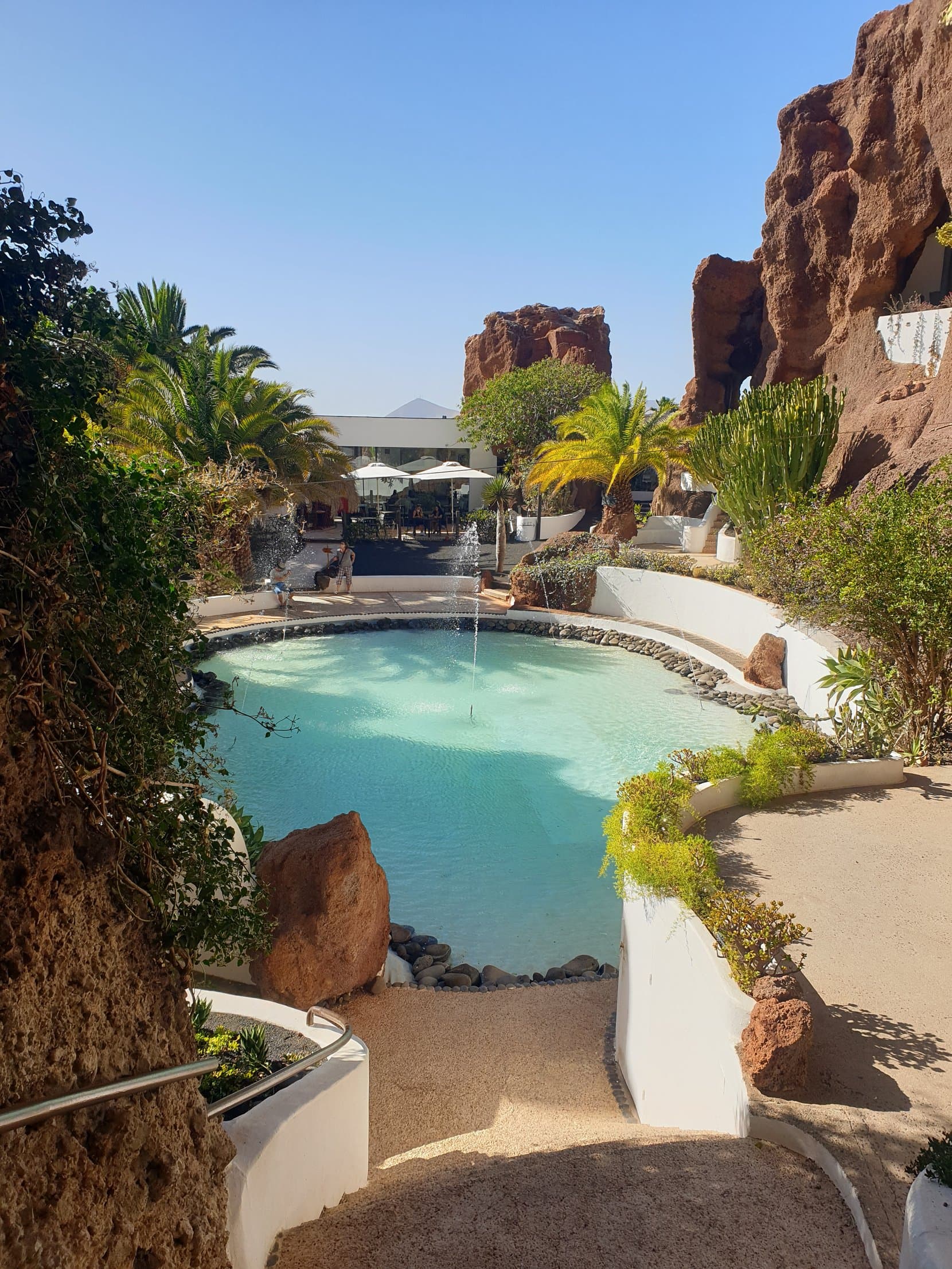 A turquoise pool folded into red rock with palms at Lagomar, Lanzarote
