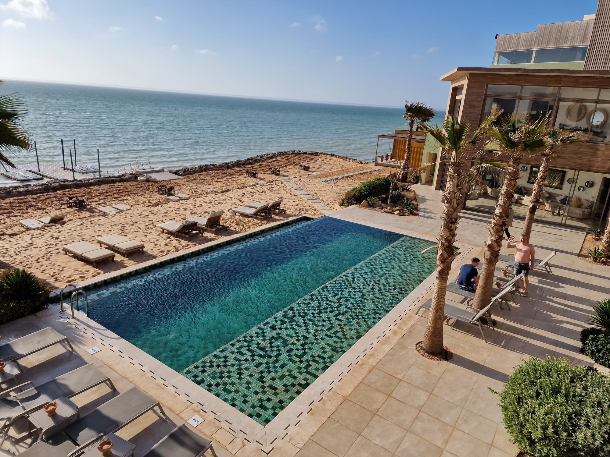 A lagoon-side hotel pool with palms and the Atlantic beyond