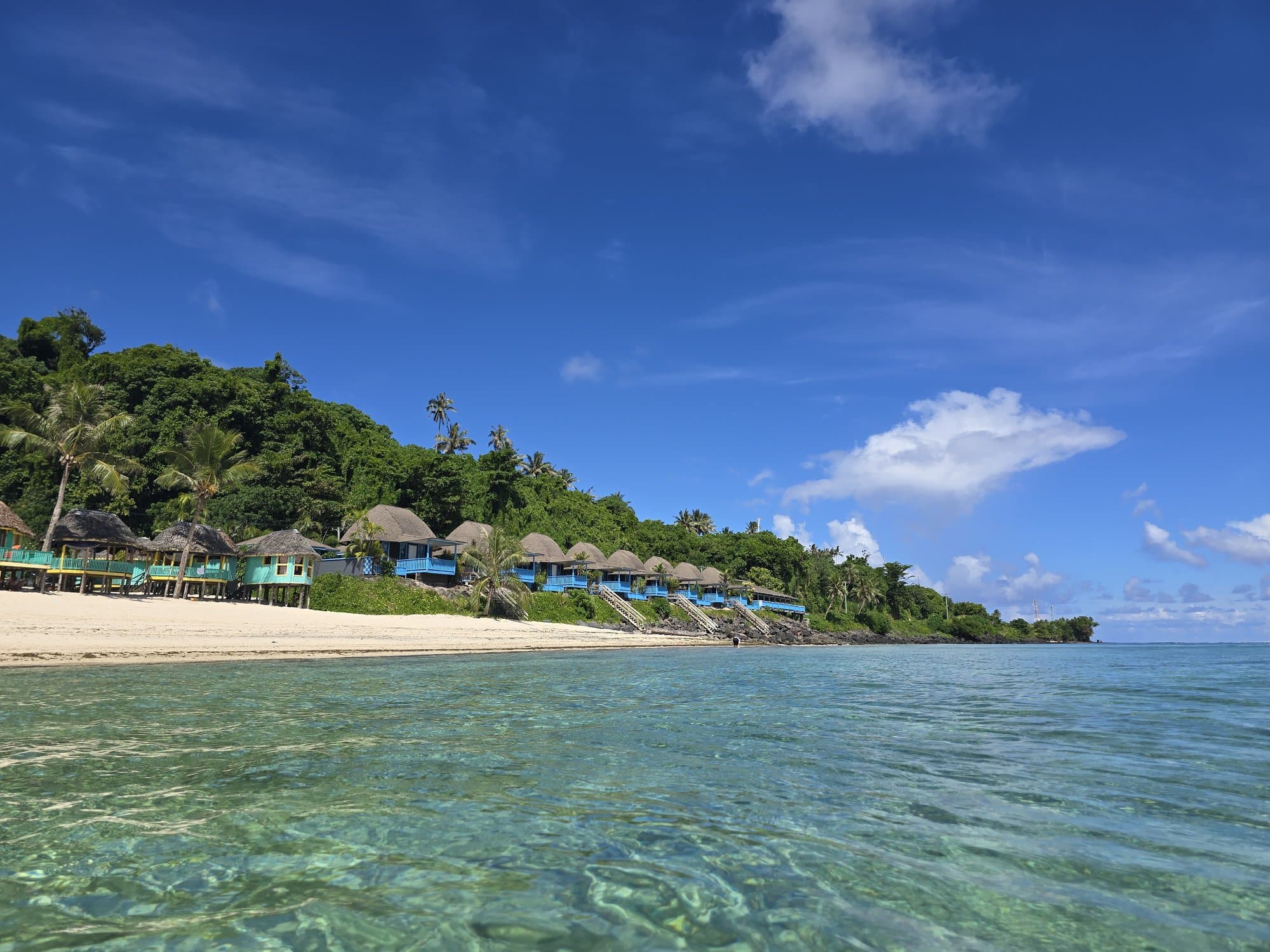 Clear turquoise shallows off a Samoan beach, fales along the shore