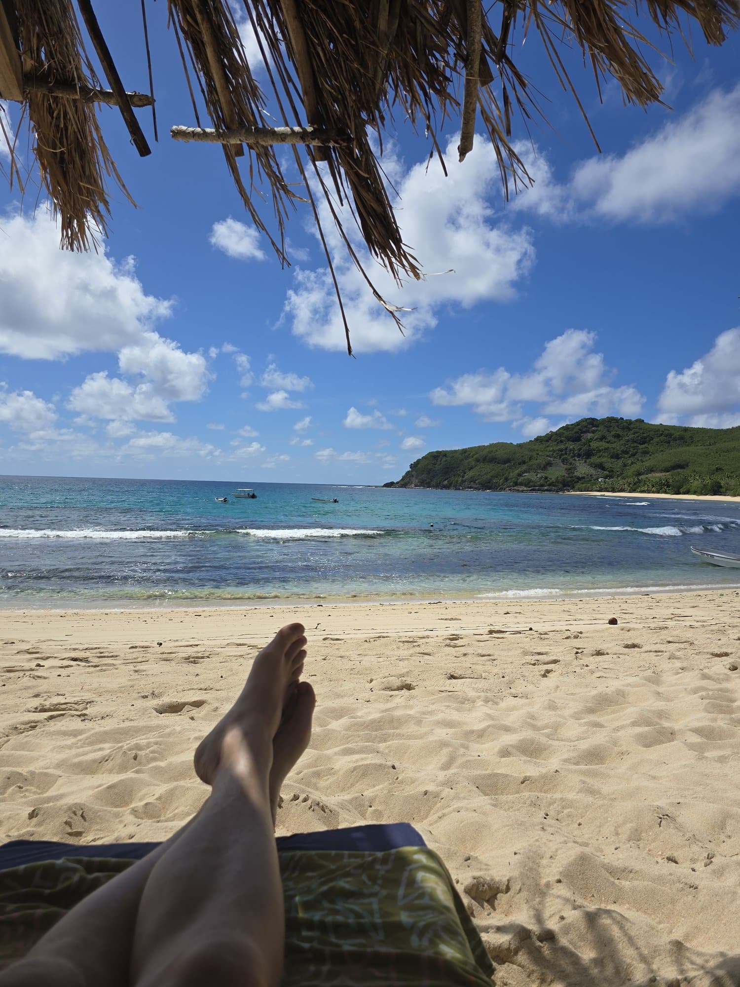 Feet up under a thatched beach shelter looking onto white sand and sea