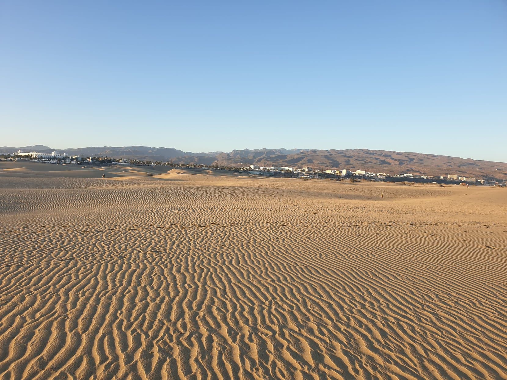Rippled sand dunes running toward the resort strip and mountains at Maspalomas, Gran Canaria
