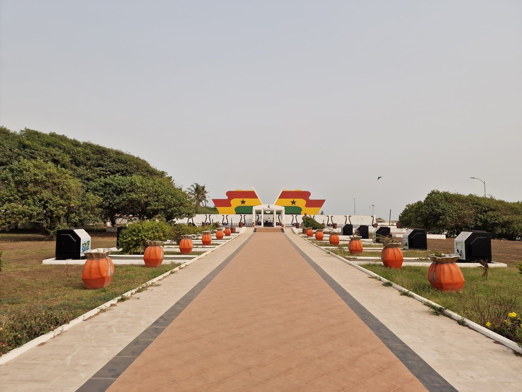 A paved memorial avenue lined with lanterns leading to a gateway in Ghana's colours, Accra