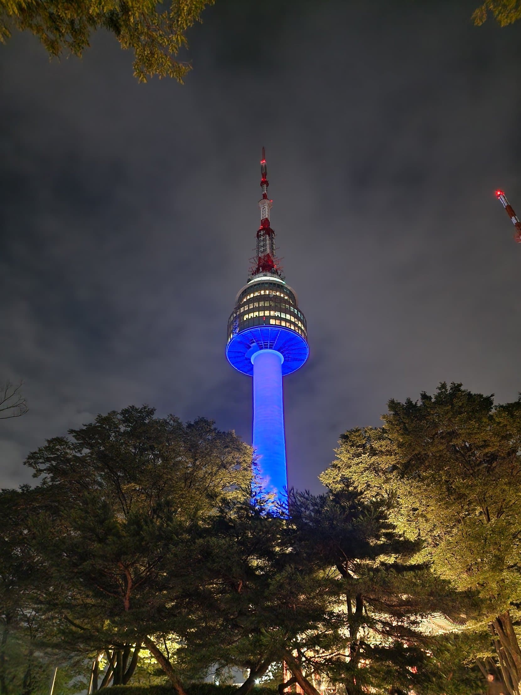 N Seoul Tower lit blue at night above pine trees on Namsan, Seoul