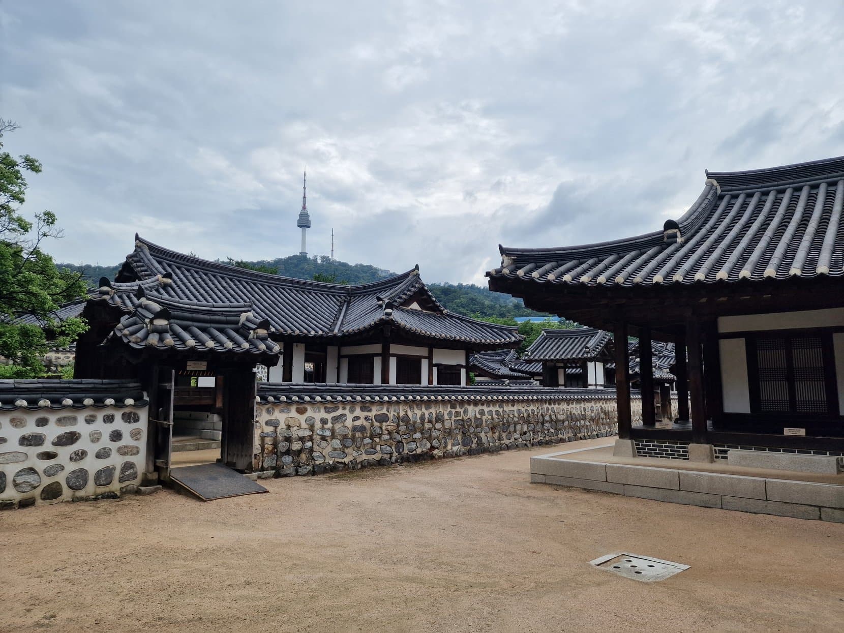 A hanok courtyard at Namsangol Hanok Village with N Seoul Tower rising behind it on Namsan, Seoul