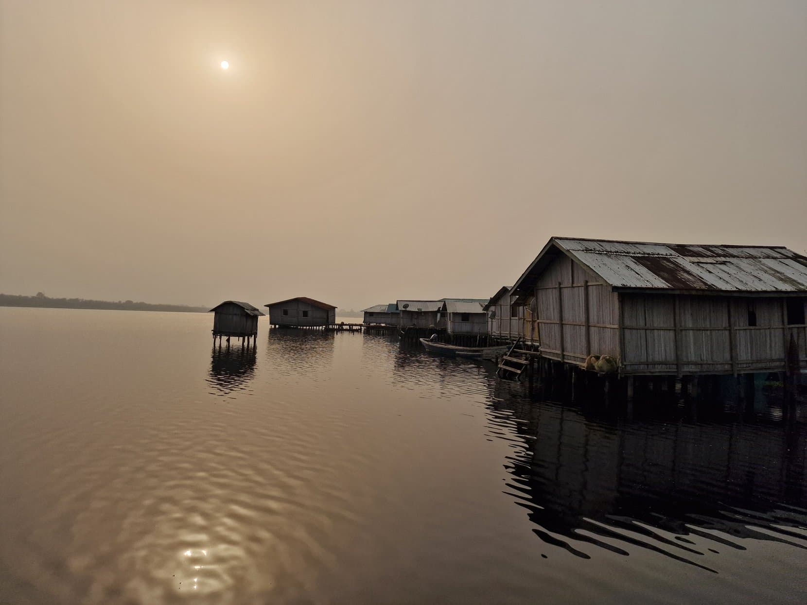 Wooden stilt houses over a still lake in morning haze, Nzulezo, Ghana