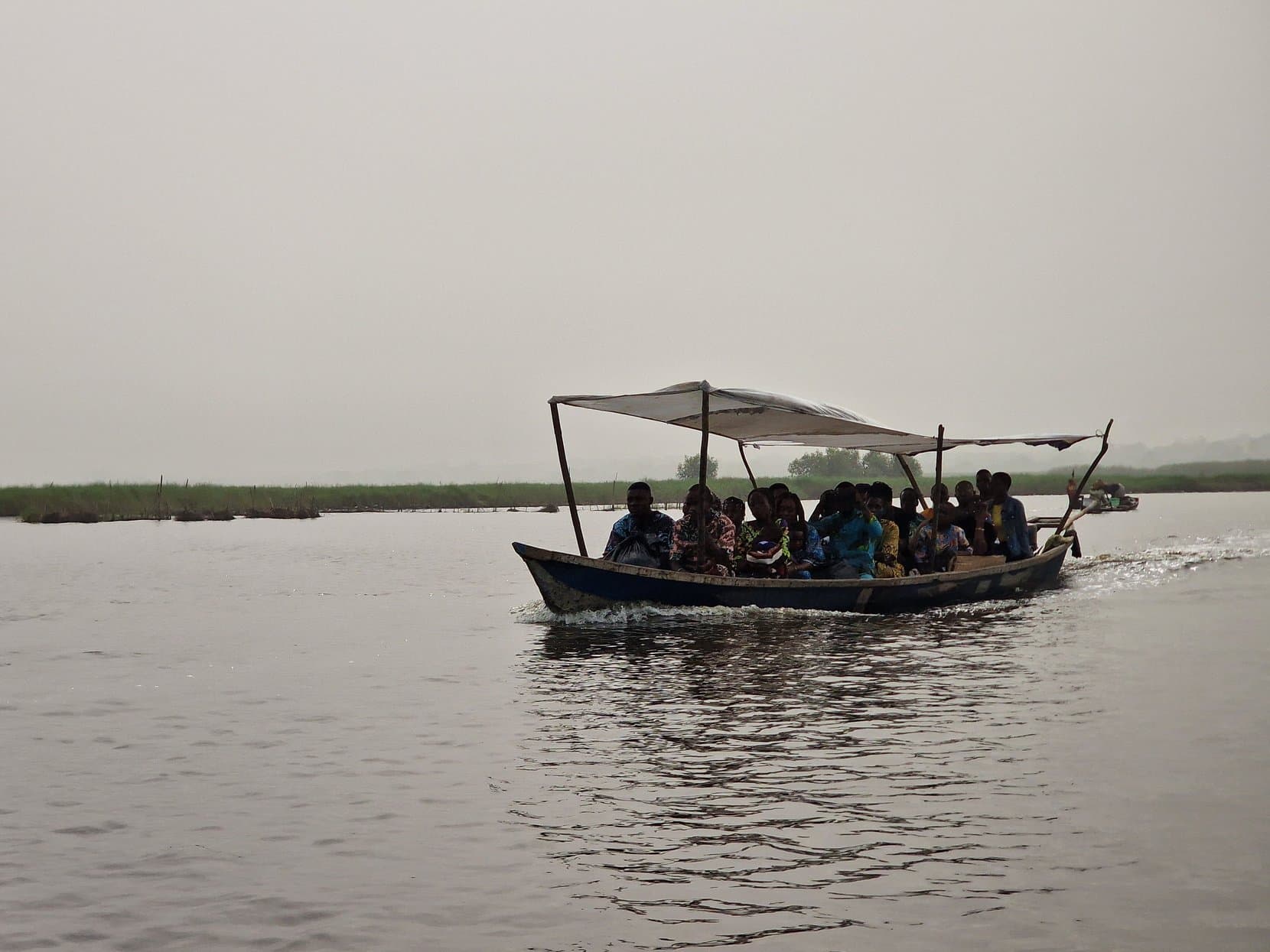 A long wooden passenger pirogue with a canopy, full of people, under way on Lake Nokoué, Benin