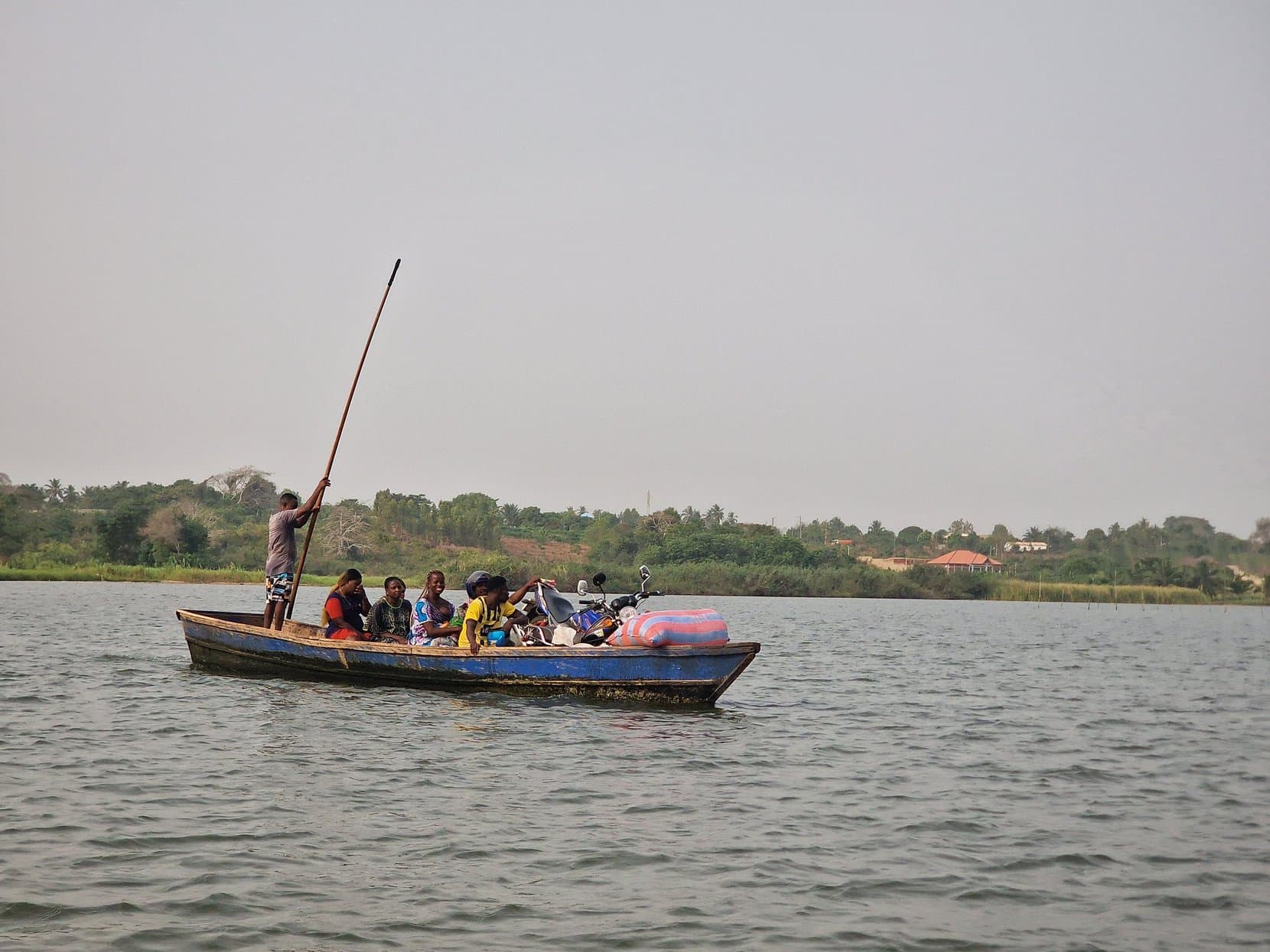 A loaded wooden boat being poled across the shallow water of Lake Togo, Togo