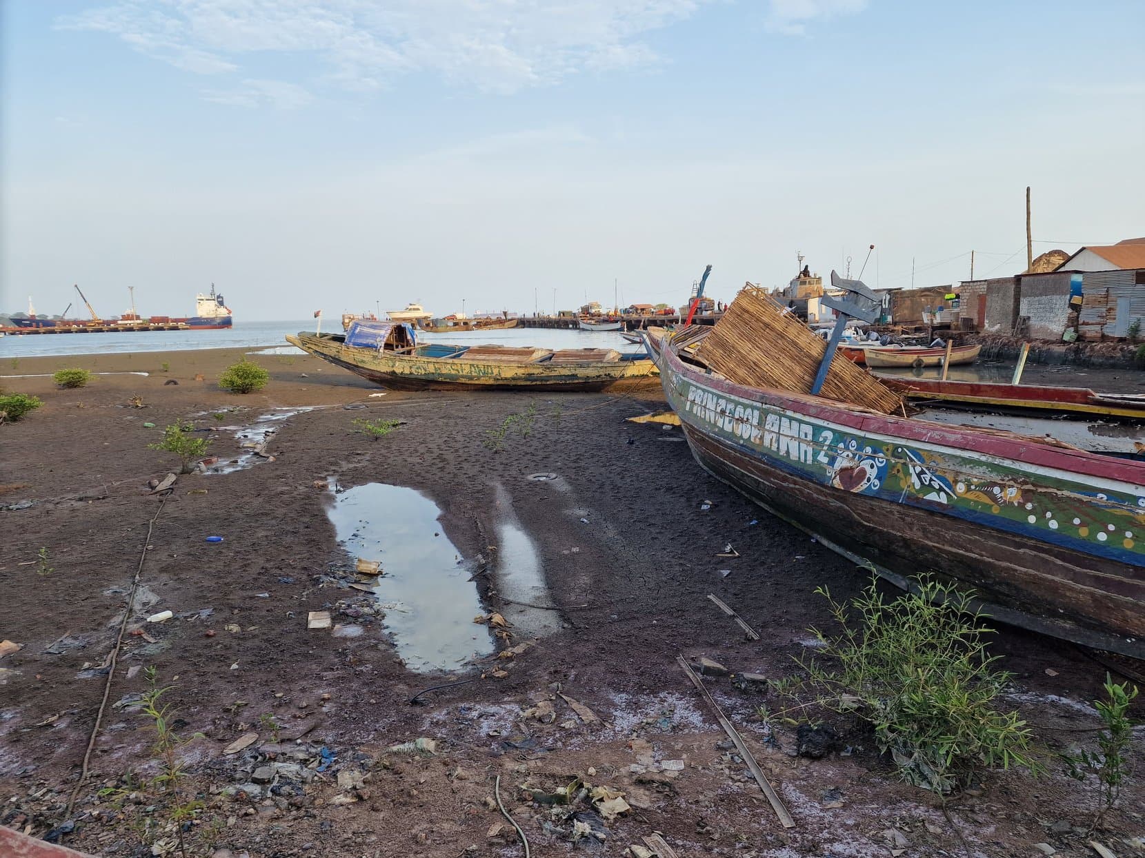 Fishing pirogues on the mudflats at low tide with the cranes of Bissau's port behind
