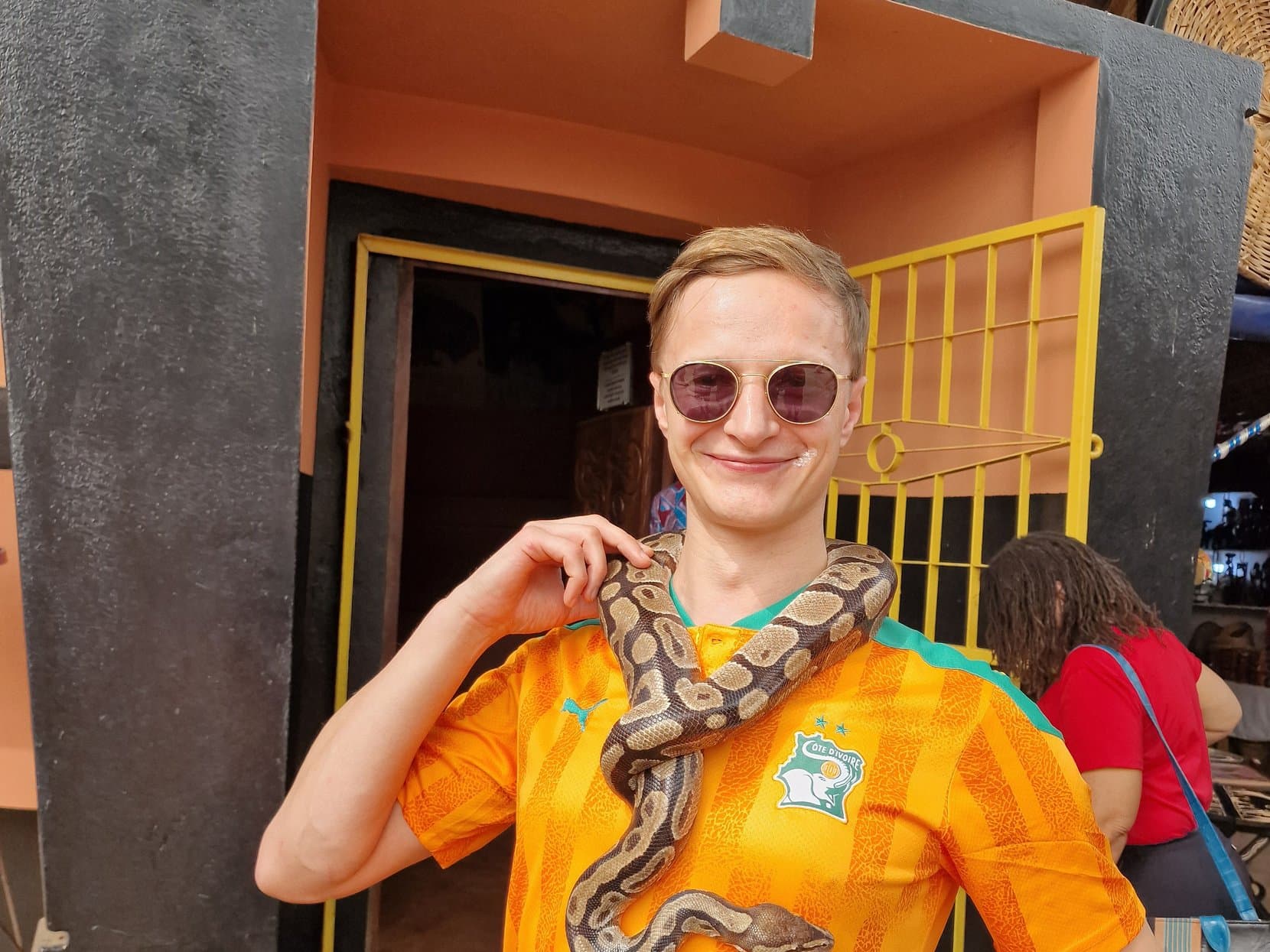 A visitor with a royal python draped round the neck in the doorway of the Temple of Pythons, Ouidah, Benin