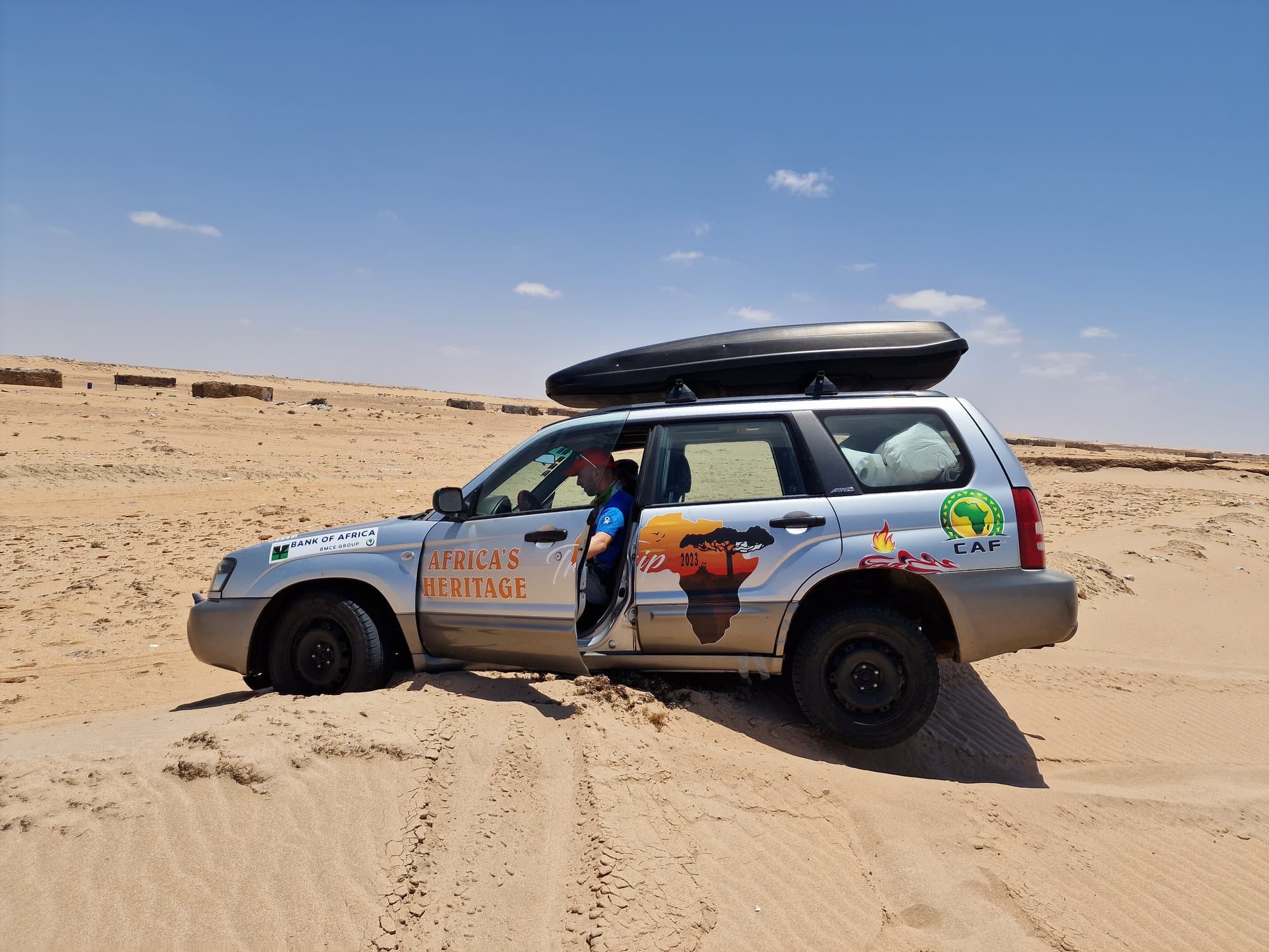 A rally car with a roof box parked on soft beach sand