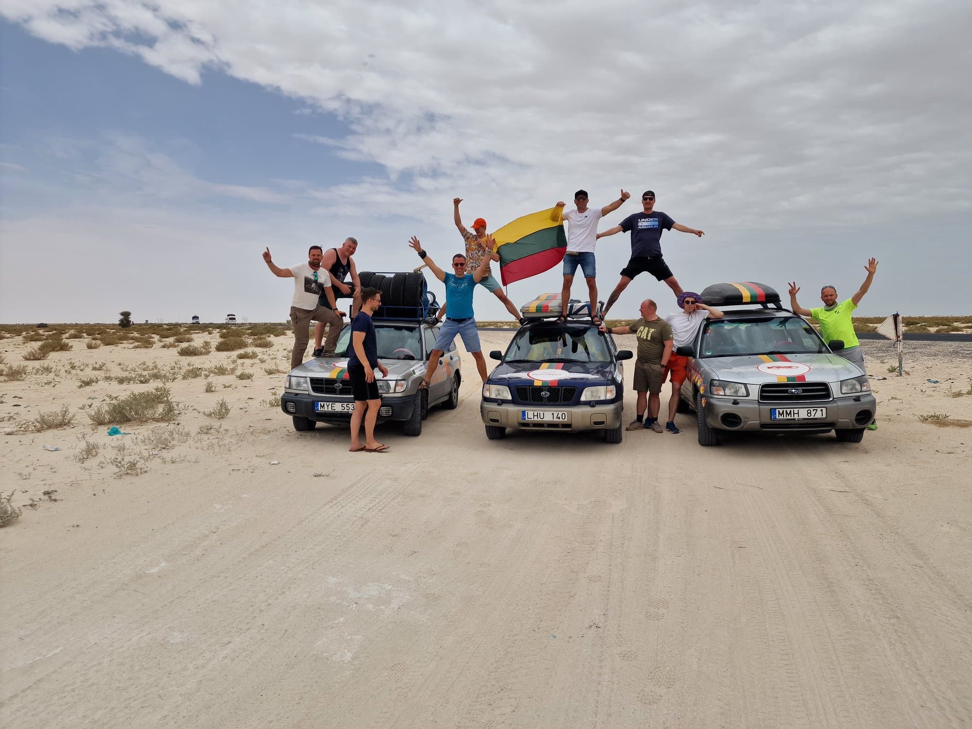 The crew celebrating on their cars with a Lithuanian flag in the dunes