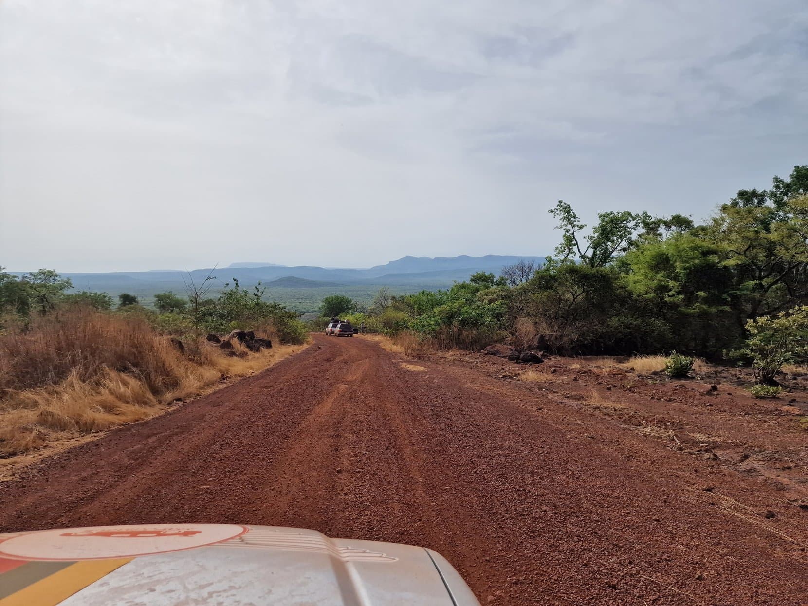 A red laterite road running downhill toward the blue hills of the Fouta Djallon, Guinea