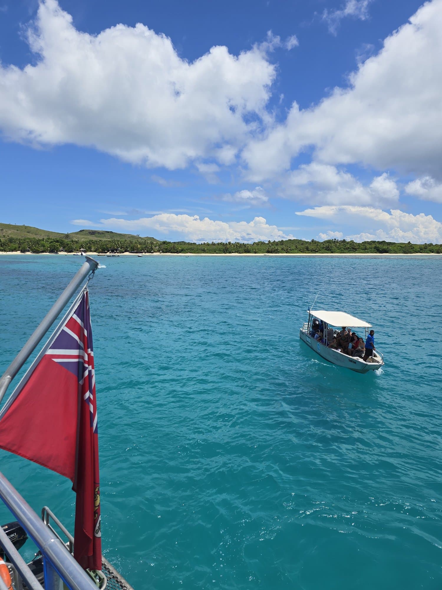 A small resort boat on turquoise water, a red ensign at the stern