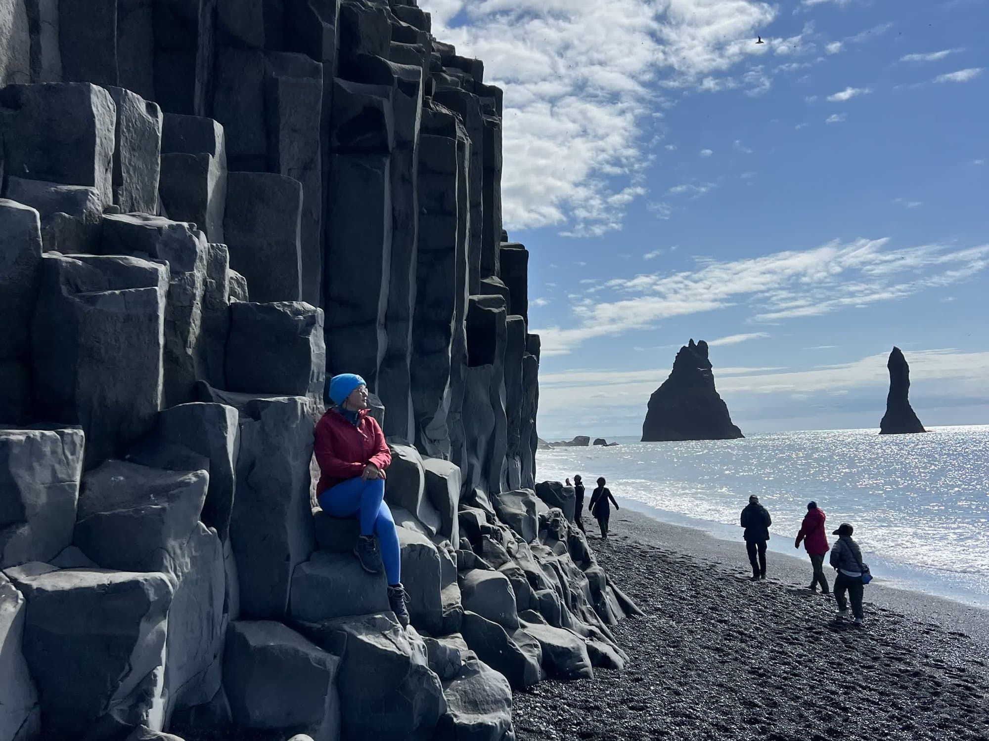 Basalt columns at Reynisfjara with walkers on the black sand and the Reynisdrangar stacks beyond