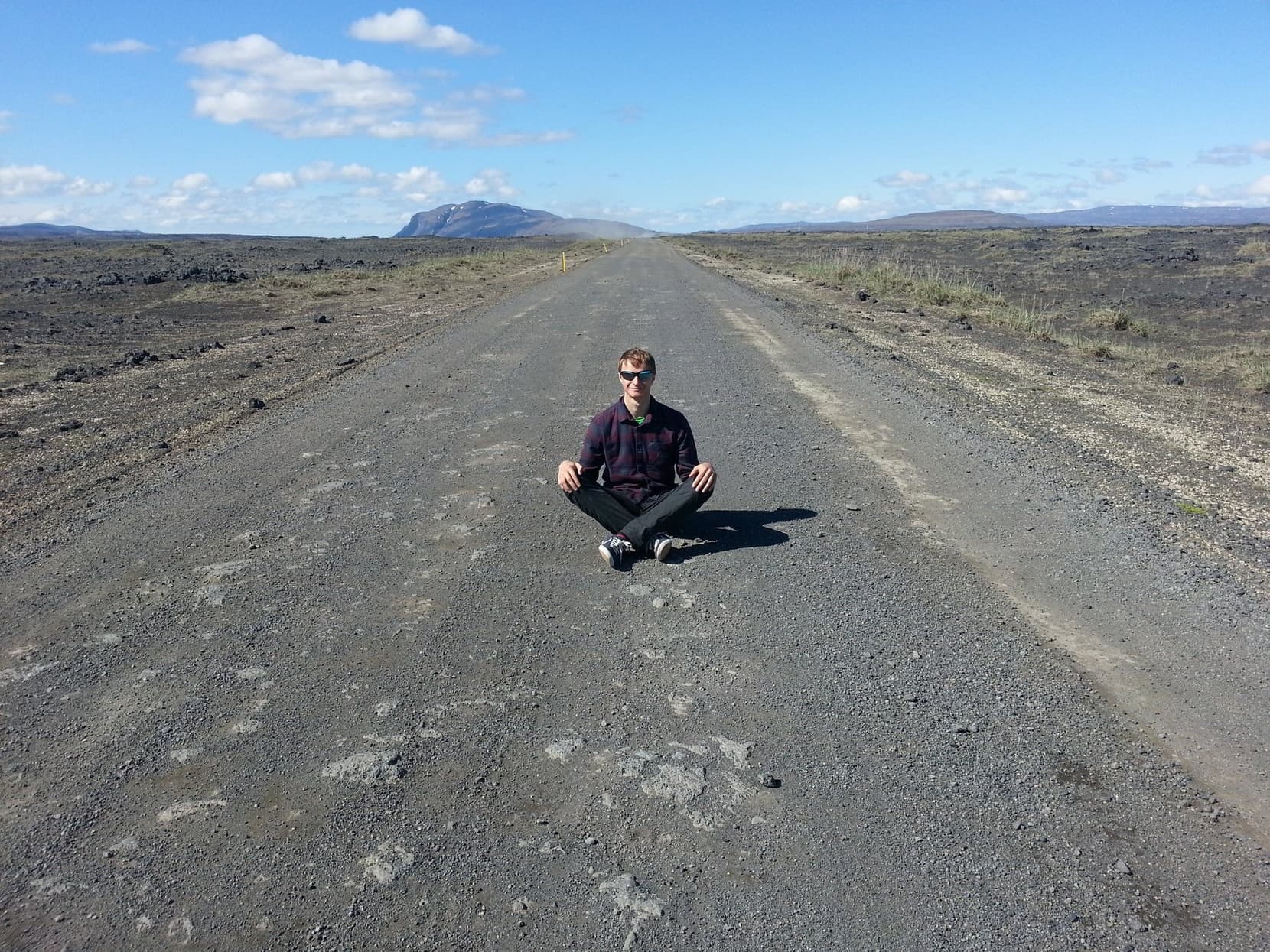 Sitting cross-legged in the middle of an empty gravel road with a mountain beyond