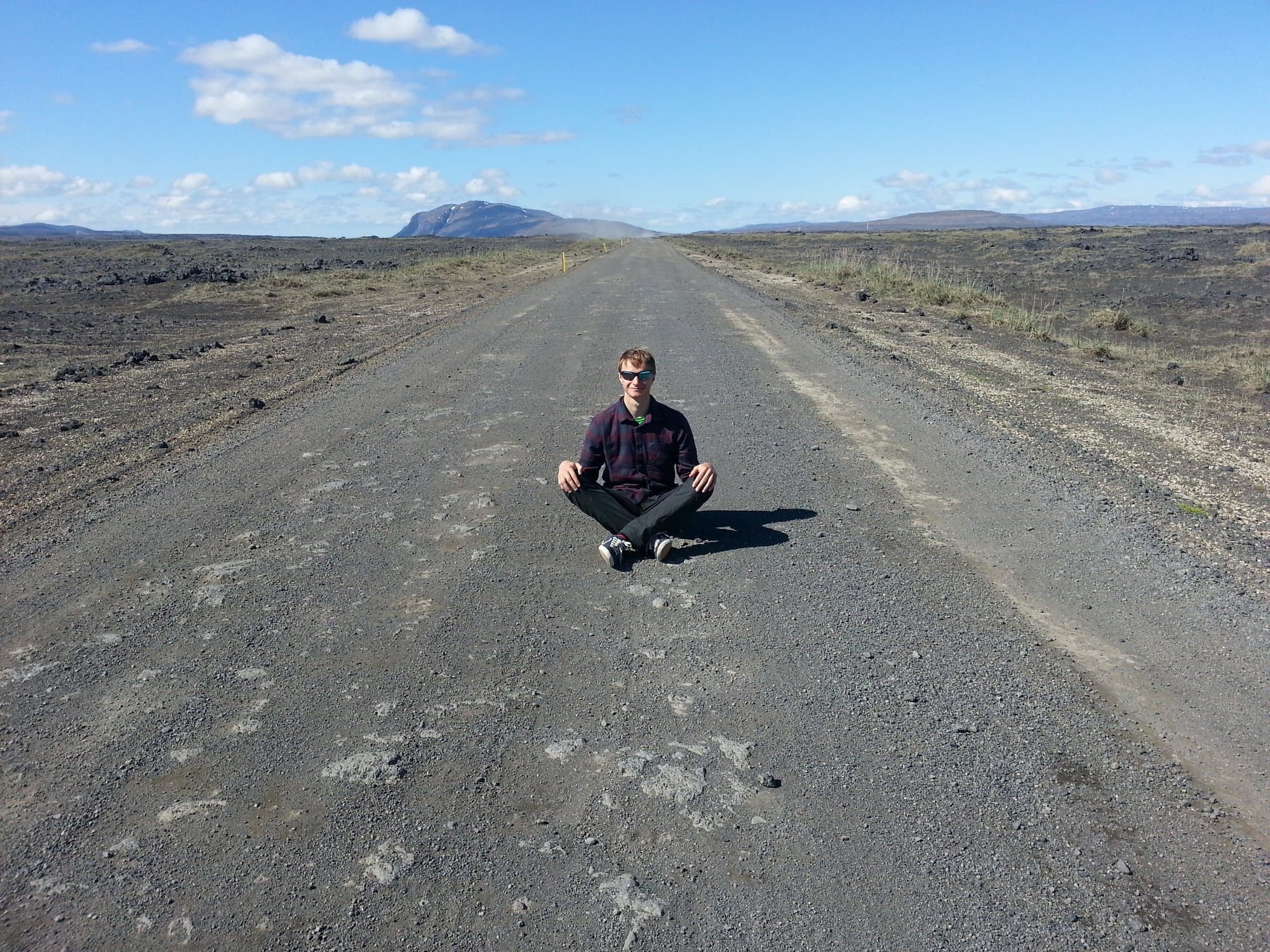 Sitting cross-legged in the middle of an empty gravel road with a mountain beyond