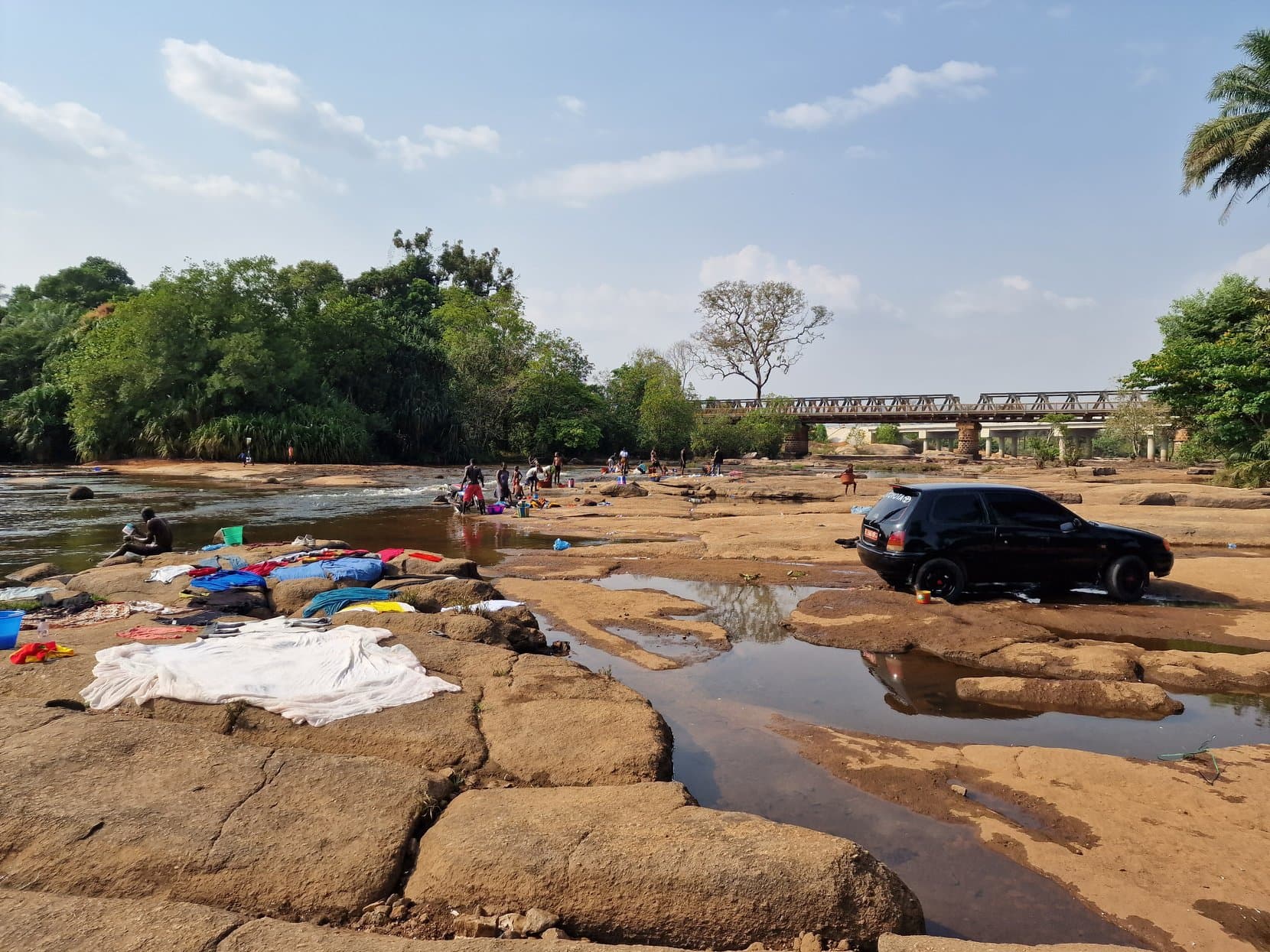 Washing spread to dry on river rocks below an iron truss bridge, Guinea