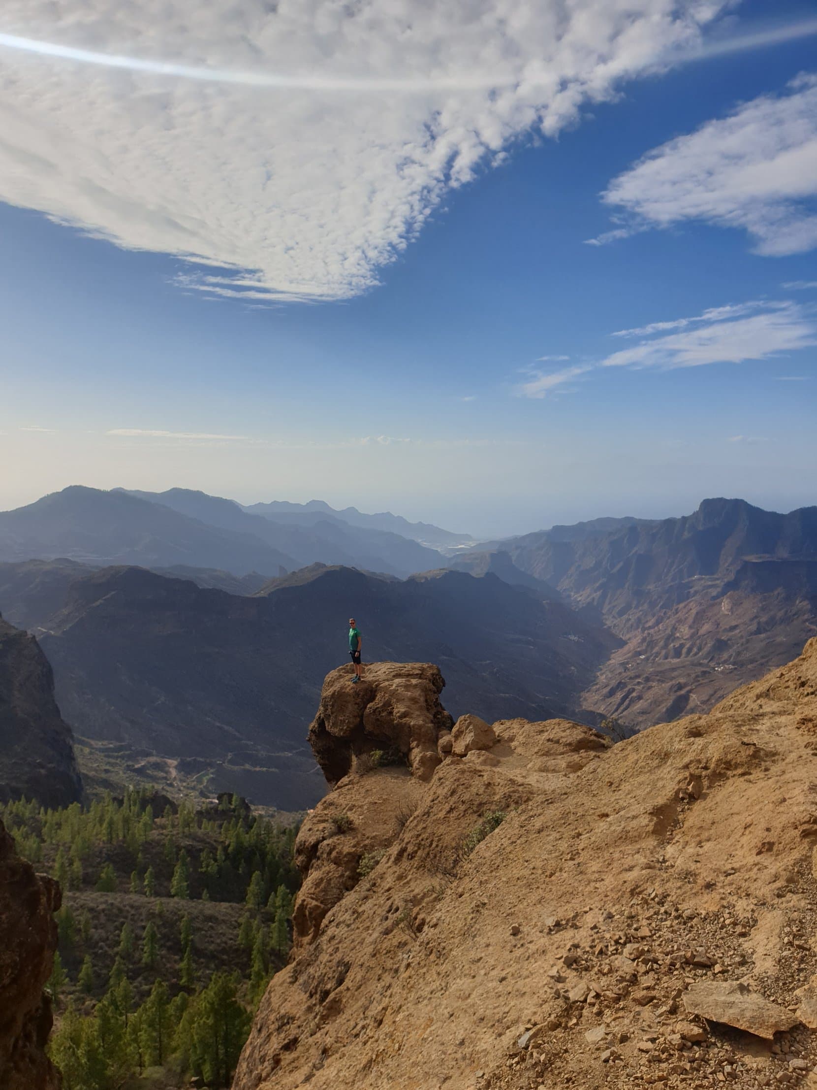 A hiker on the balcony rocks beside Roque Nublo, ridges fading behind, Gran Canaria